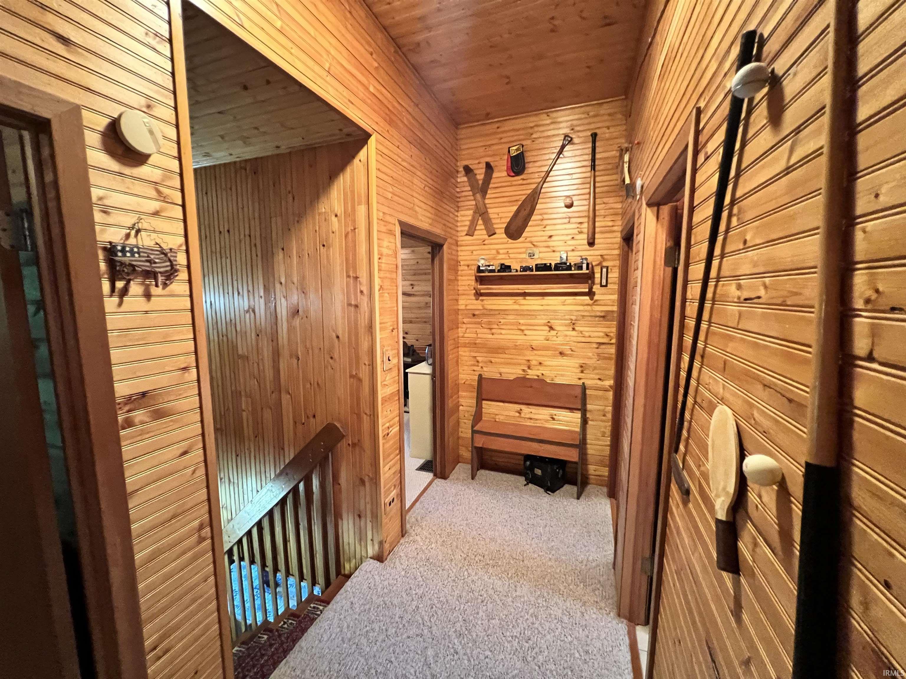 Wood-paneled hallway featuring light-colored carpeting, multiple doorways, and a wooden staircase with a balustrade