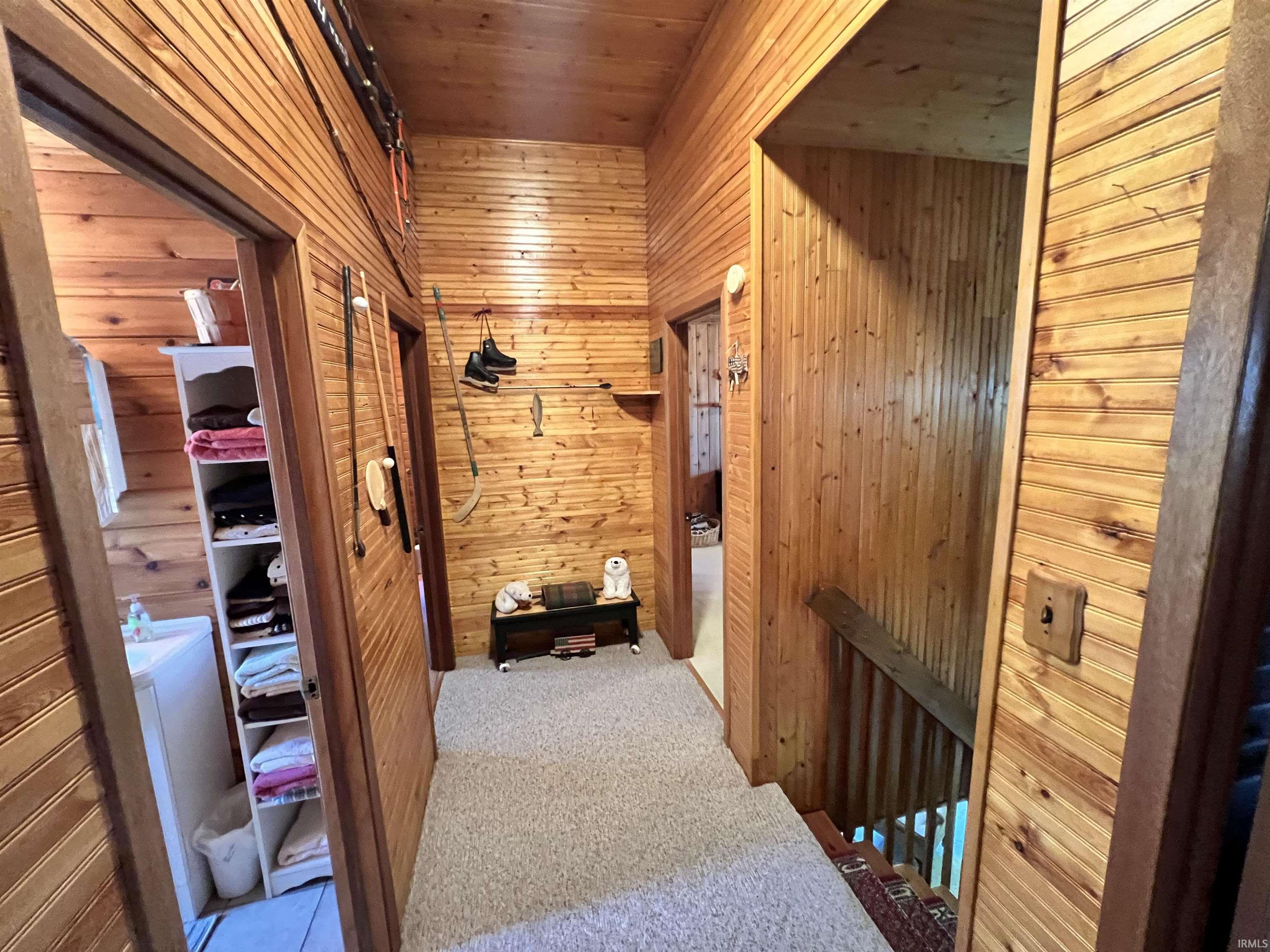Interior hallway featuring wood-paneled walls and ceiling, carpeted flooring, and wood trim around doorways