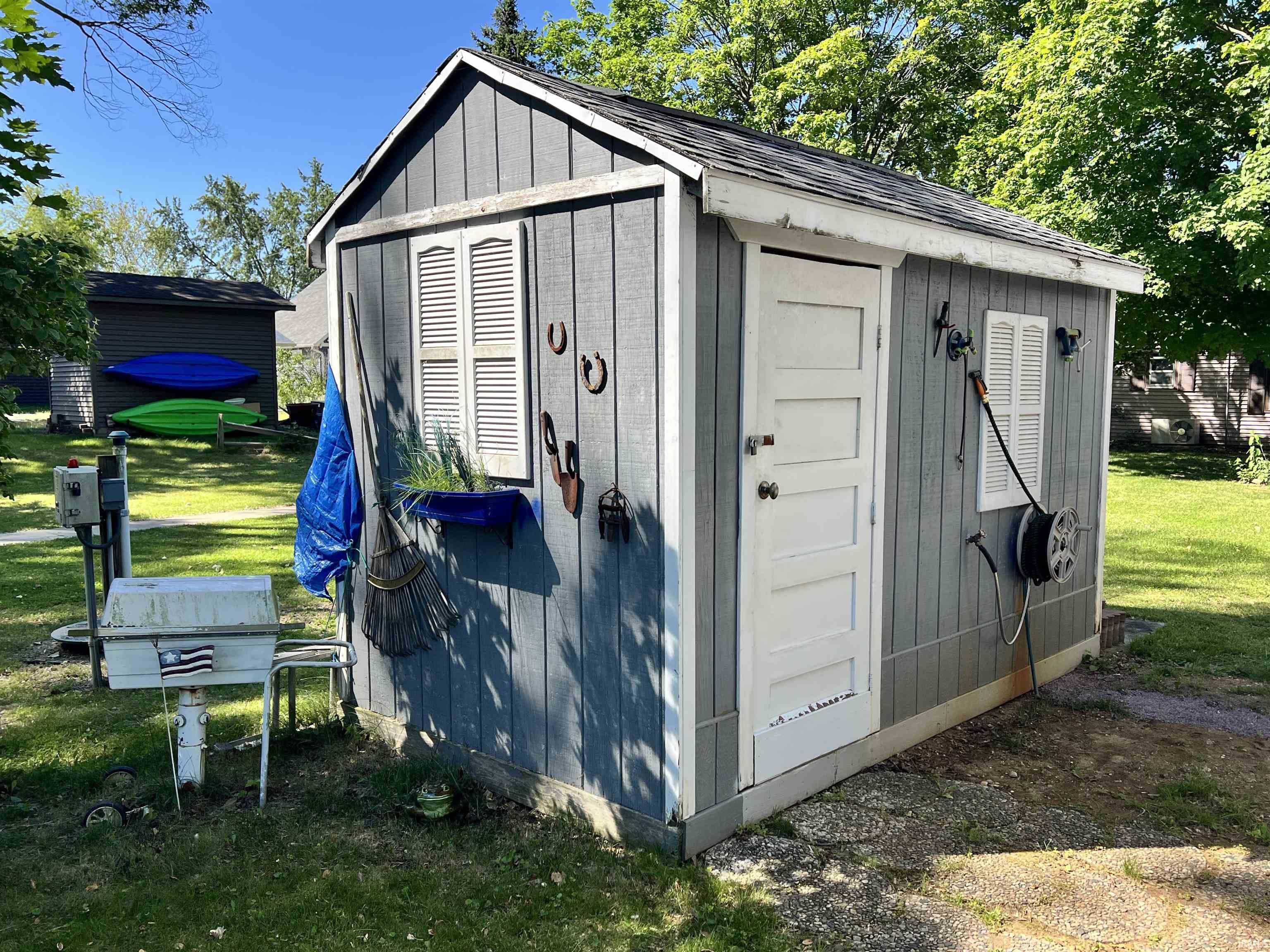 Gable-roofed utility shed featuring horizontal siding, white trim, and a panel door