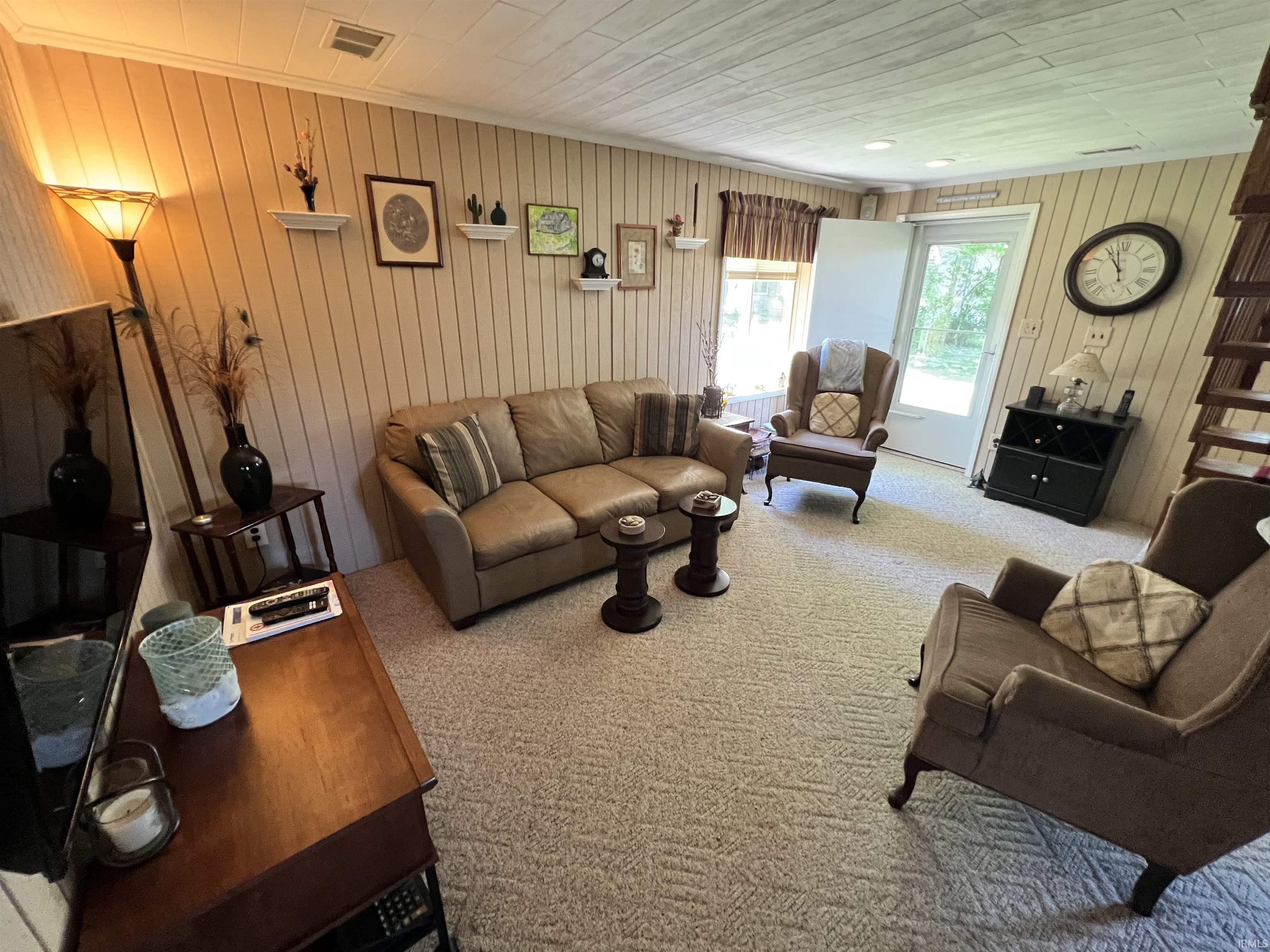 Carpeted living area featuring paneling on walls, a white paneled ceiling, and a glass-paned door providing outdoor access