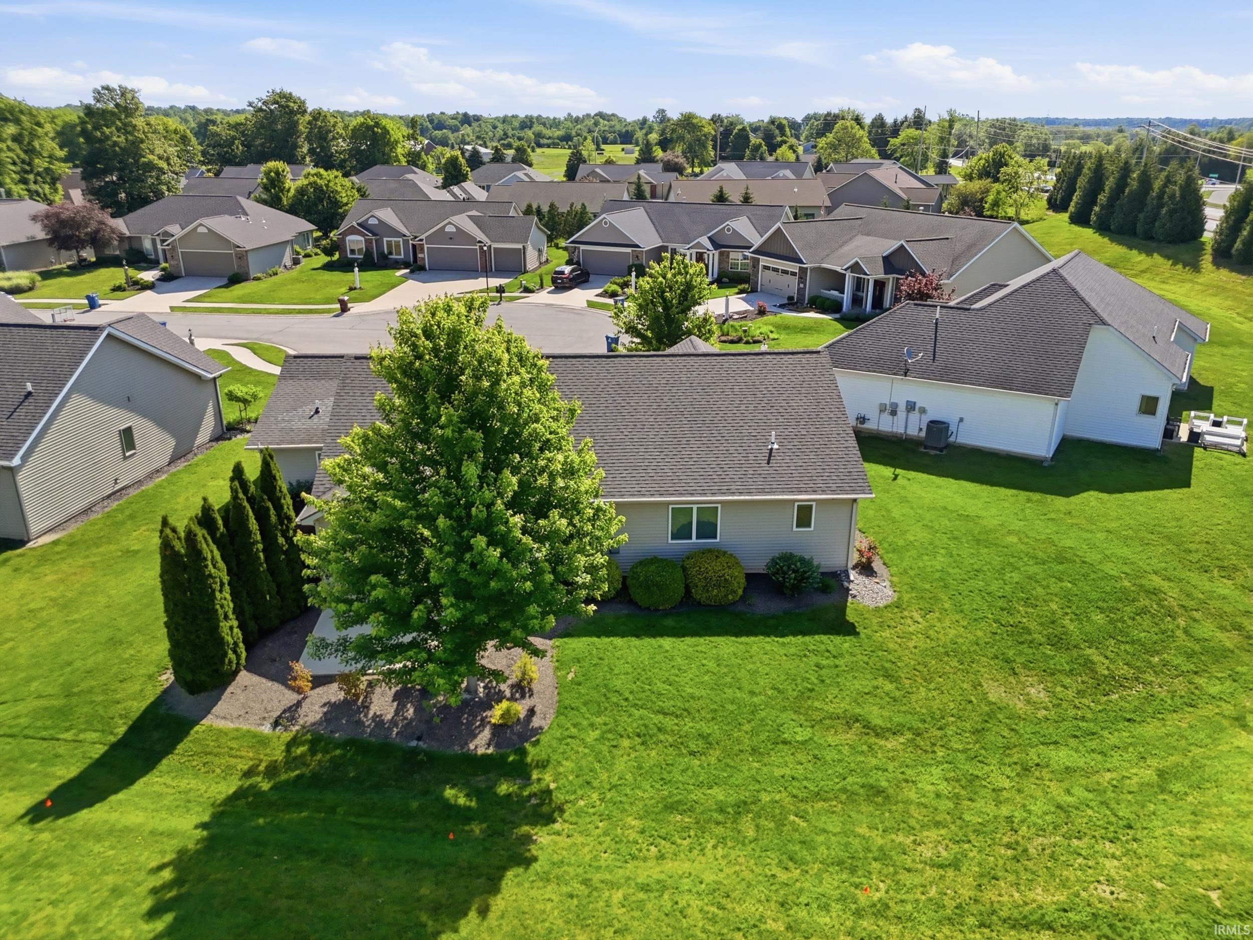 Expansive residential backyard featuring a manicured lawn, established shade tree, and well-maintained shrubs