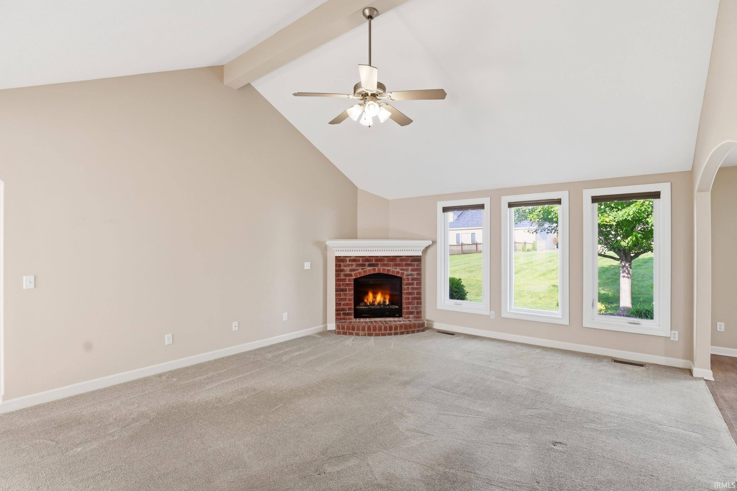 Living area featuring a vaulted ceiling with exposed beam, a corner brick fireplace with a white mantel, and three large windows