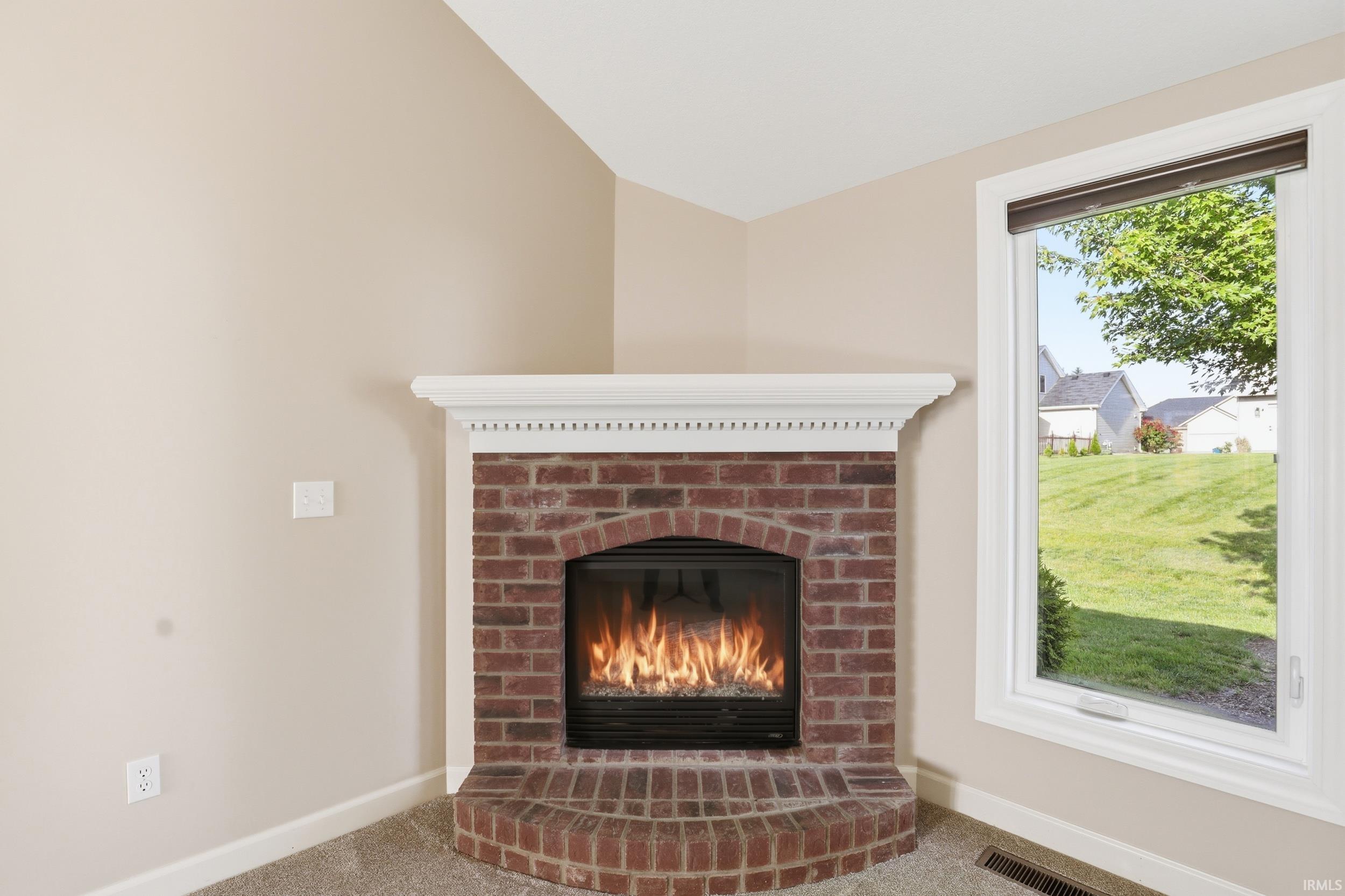 Corner fireplace featuring a brick surround, arched firebox, and a white mantel