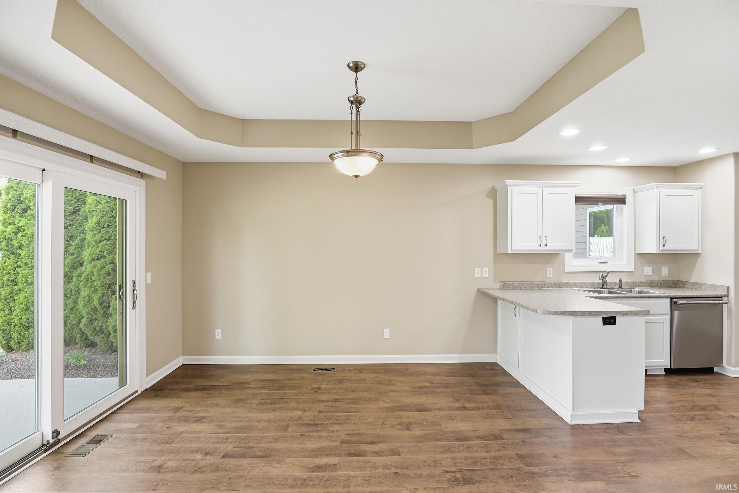 Open-concept living space featuring wood-finish flooring and a tray ceiling with a central pendant light fixture