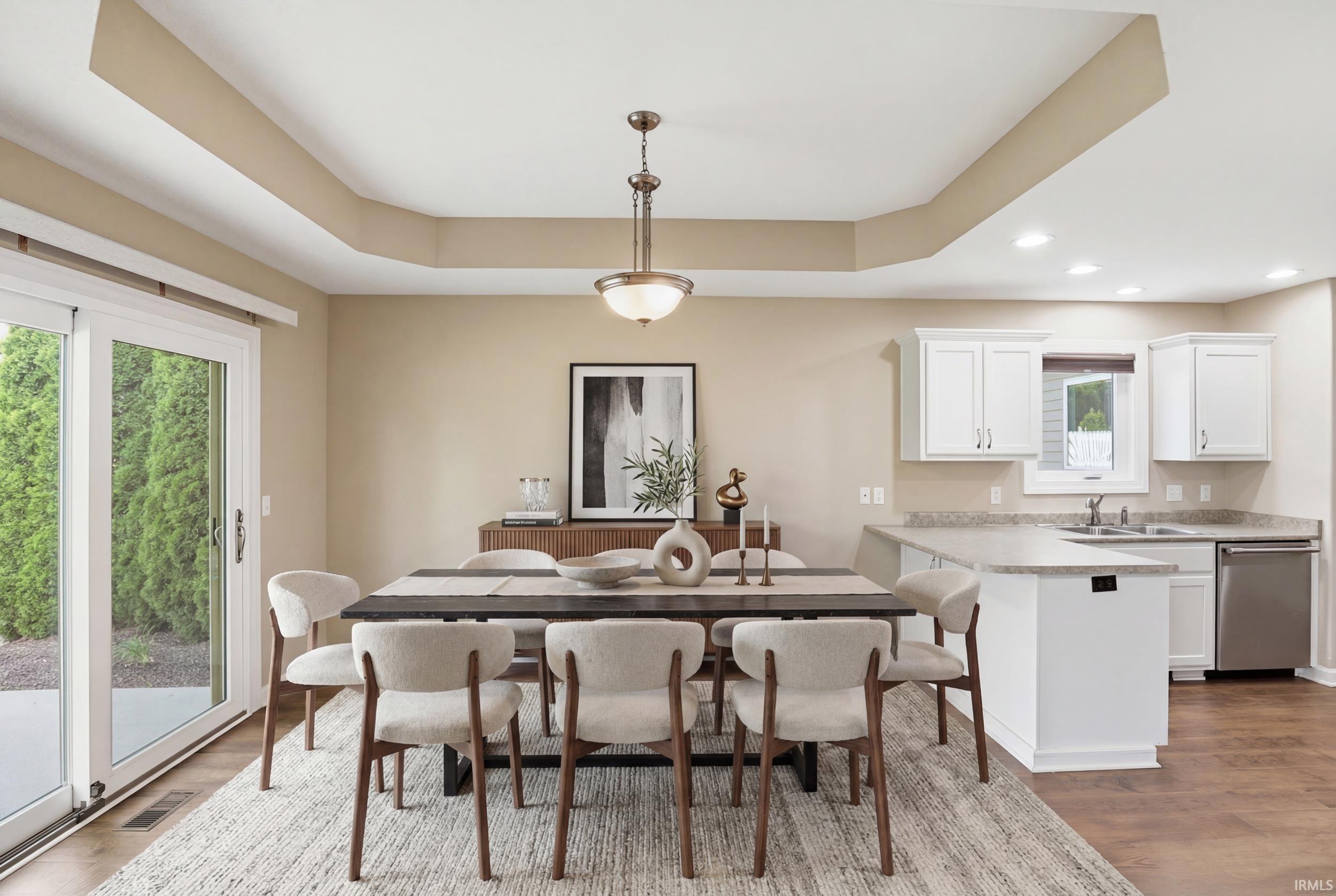 Open-concept dining area featuring a tray ceiling with a central pendant light, wood-finish flooring, and direct patio access through sliding glass doors