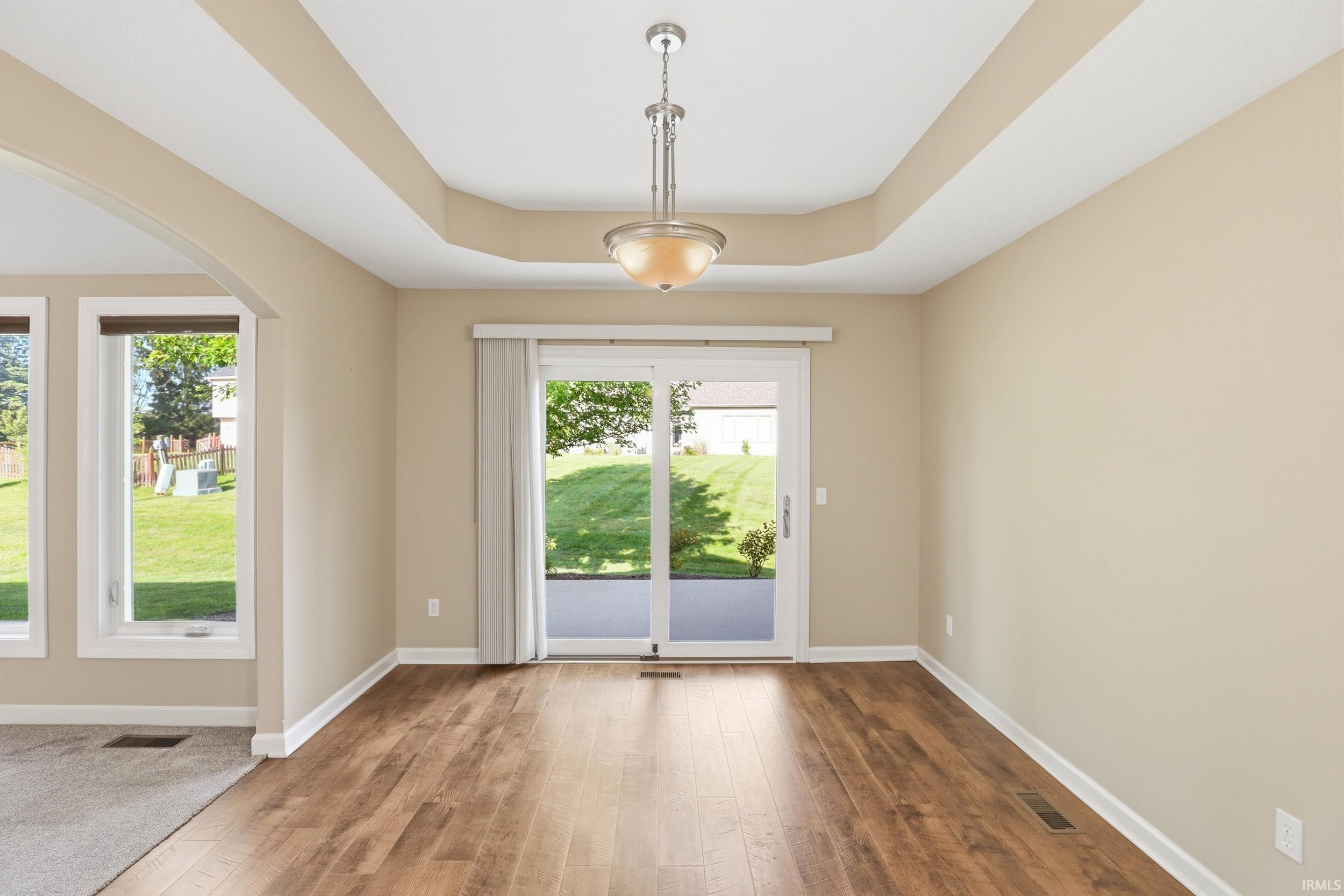 Dining area featuring wood-finish flooring, a tray ceiling with a hanging light fixture, and a sliding glass door leading to a patio