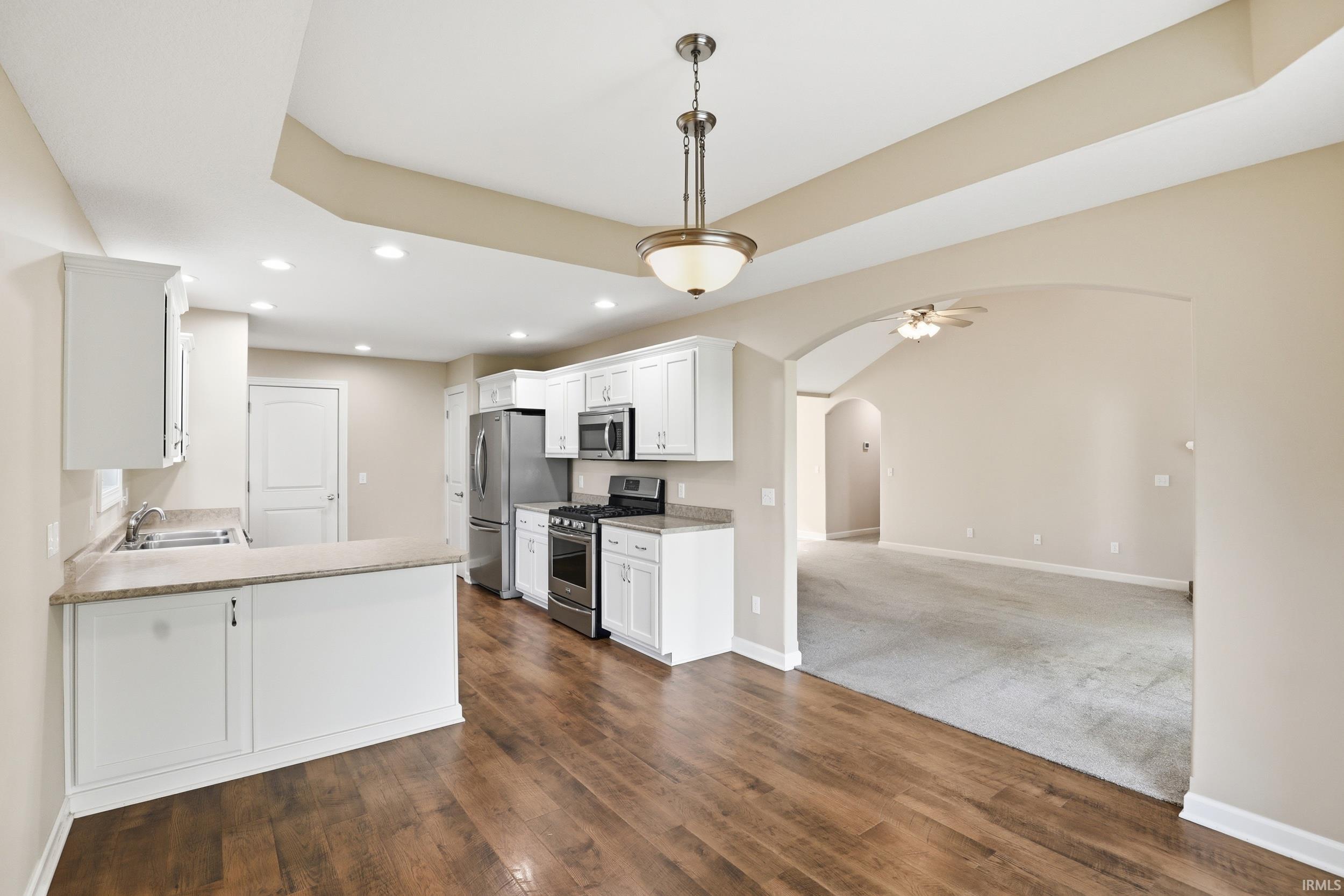 Kitchen featuring white cabinetry, stainless steel appliances, wood-finish flooring, recessed lighting, and a breakfast bar