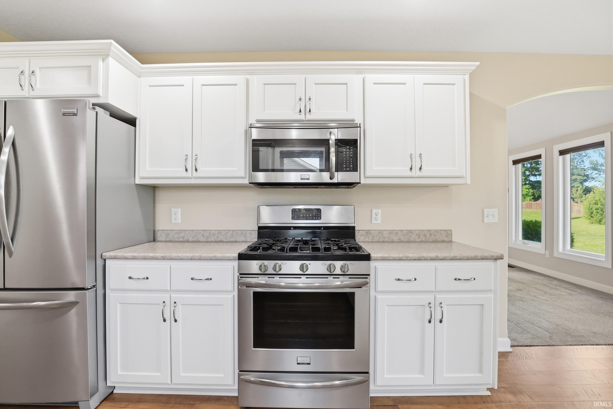 Kitchen featuring white cabinetry, stainless steel appliances, speckled countertops, and wood-finish flooring