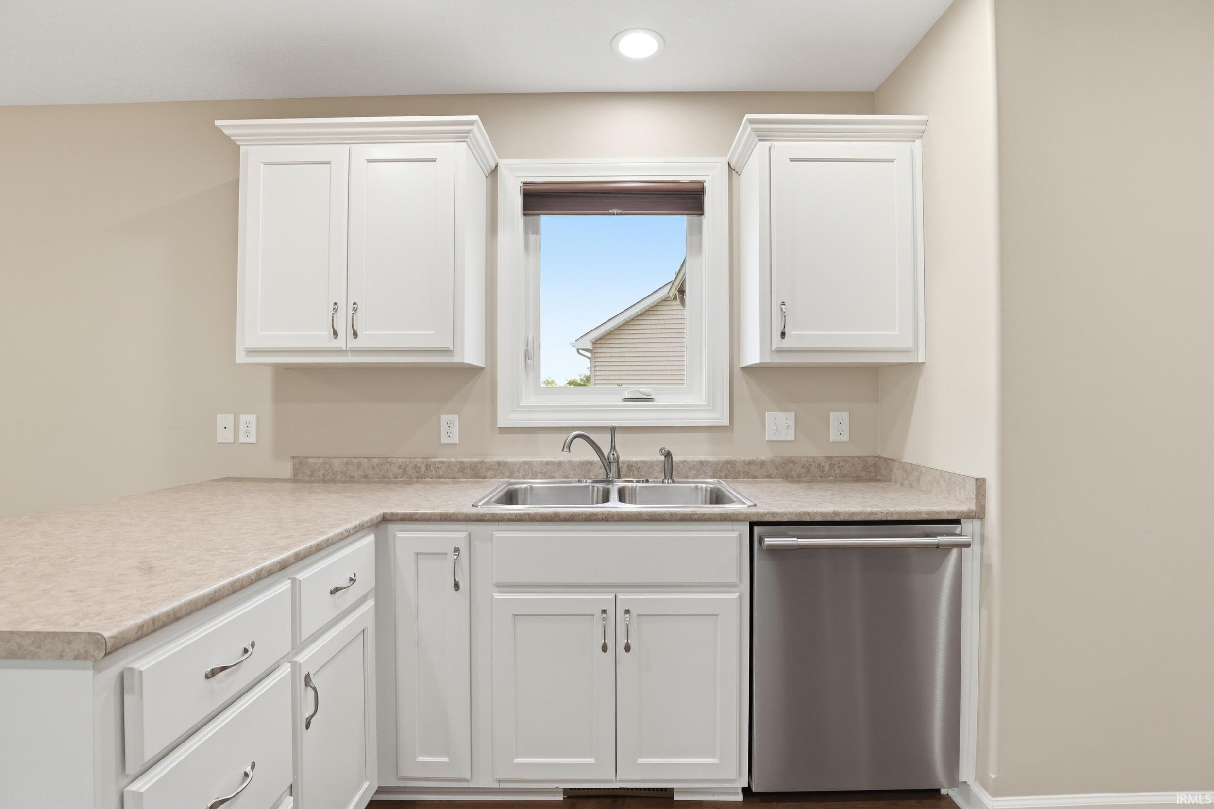 Kitchen area featuring white shaker-style cabinetry, L-shaped laminate countertops, and a double-basin stainless steel sink