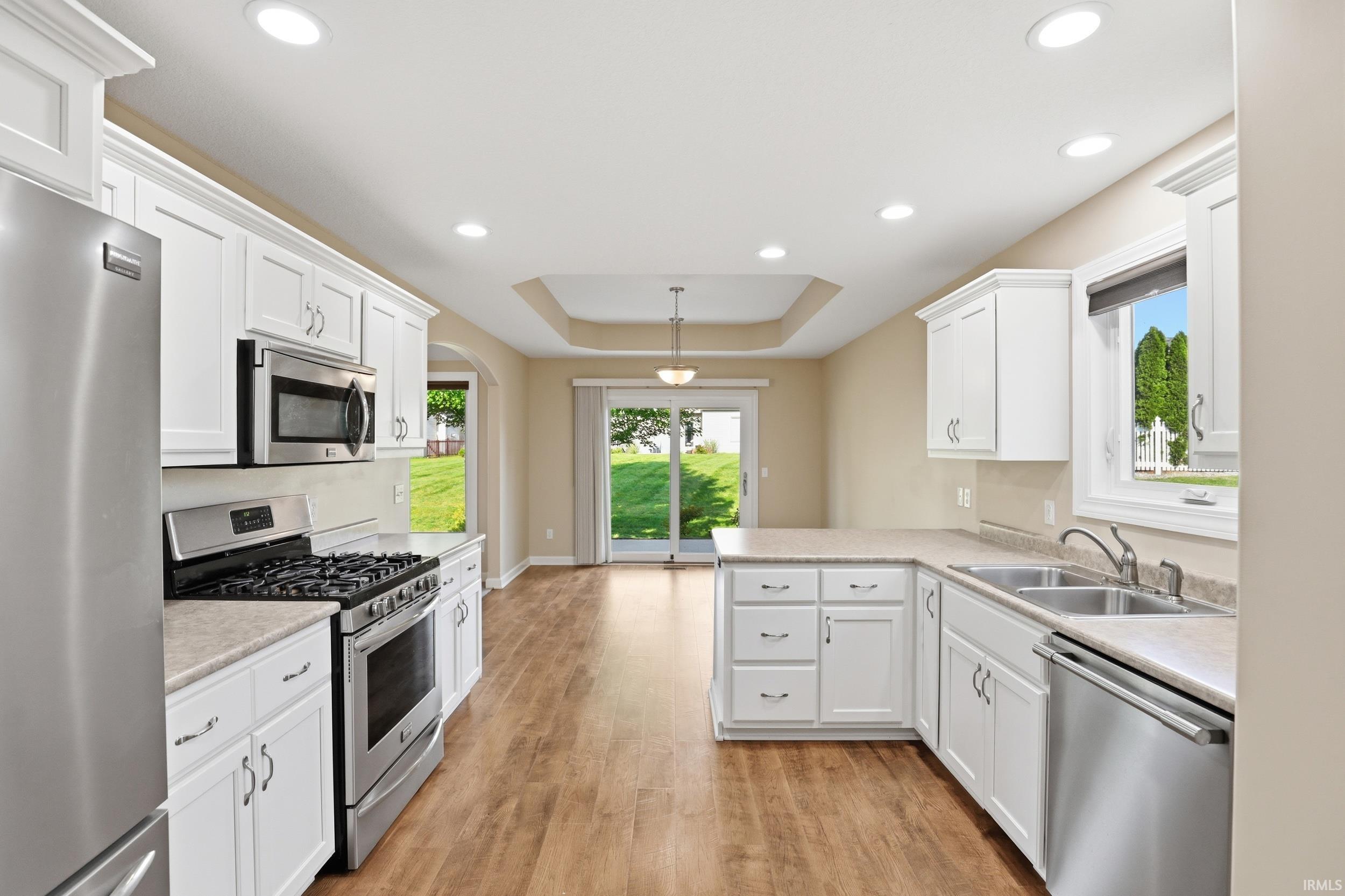 Kitchen featuring white cabinetry, stainless steel appliances, wood-finish flooring, recessed lighting, and a tray ceiling in the dining area