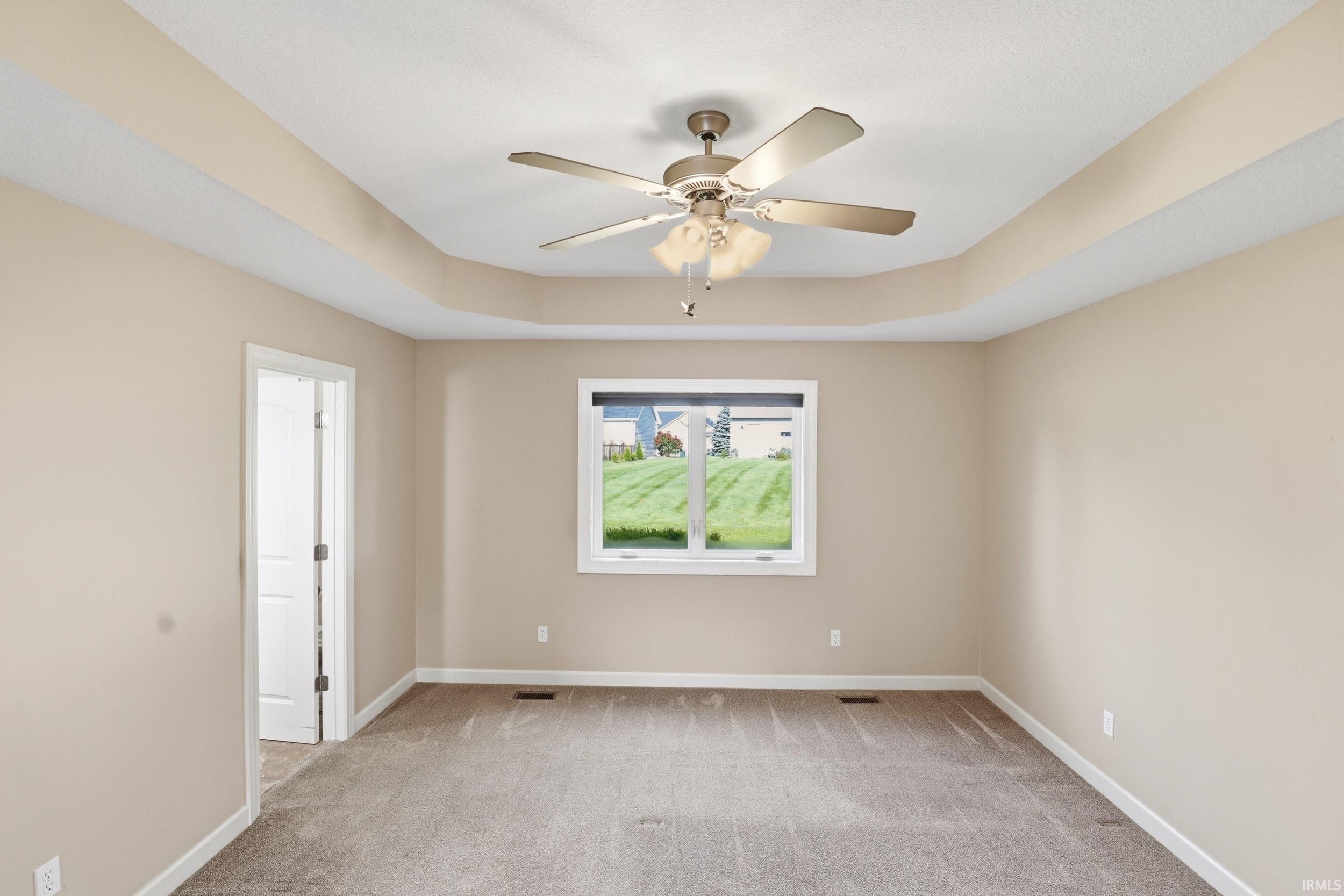 Spacious room featuring a tray ceiling with a ceiling fan, neutral wall tones, and plush carpeting