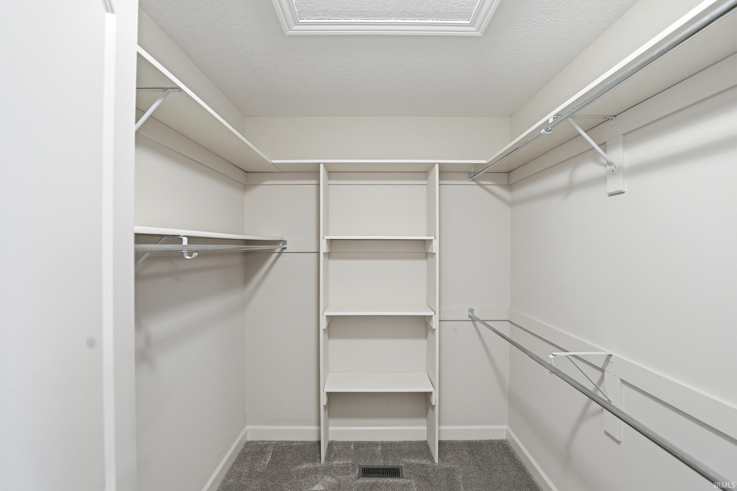 Walk-in closet featuring white built-in shelving, multiple hanging rods, and gray carpet flooring