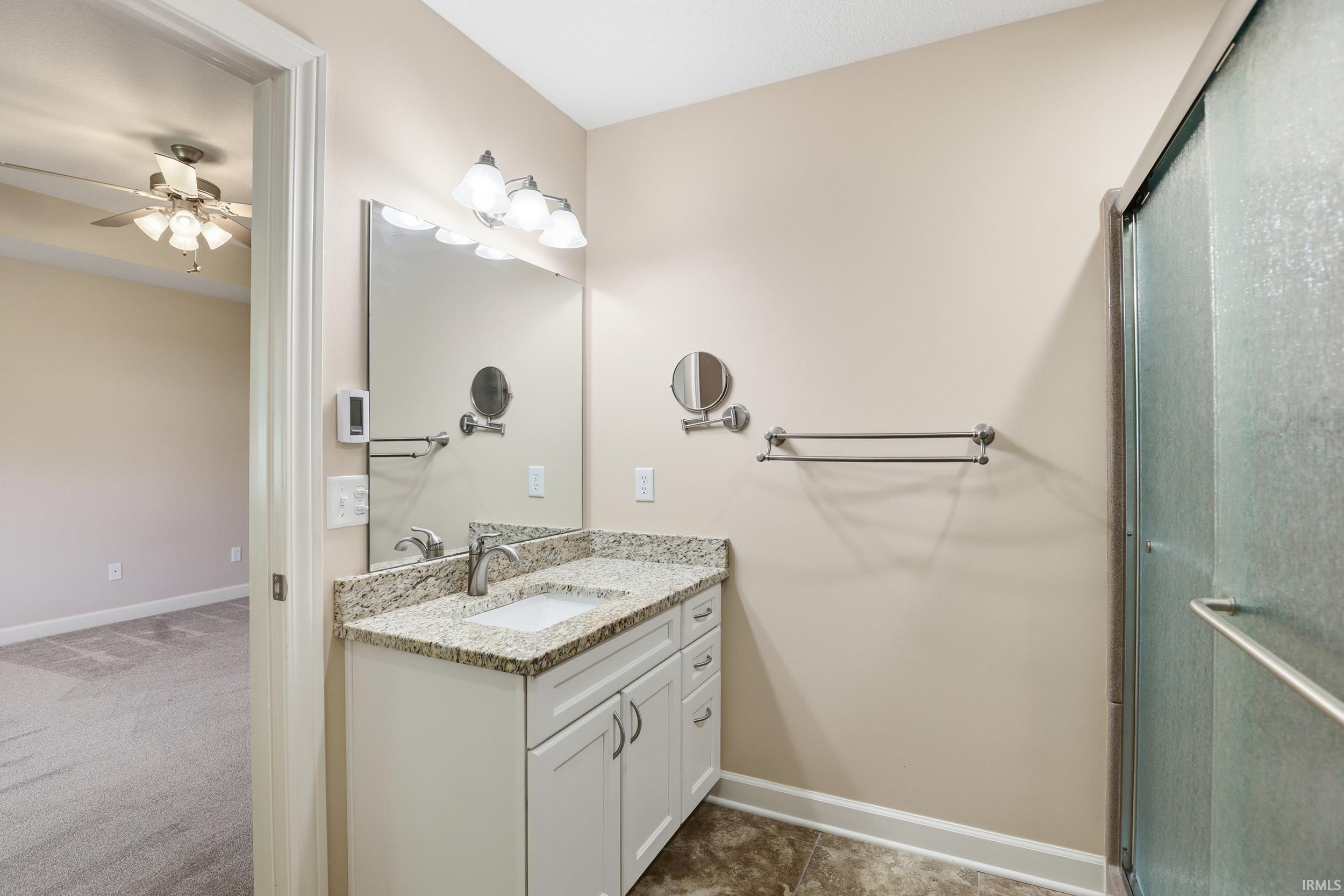Bathroom featuring a single vanity with stone-finish countertop, white cabinetry, undermount sink, and brushed nickel faucet