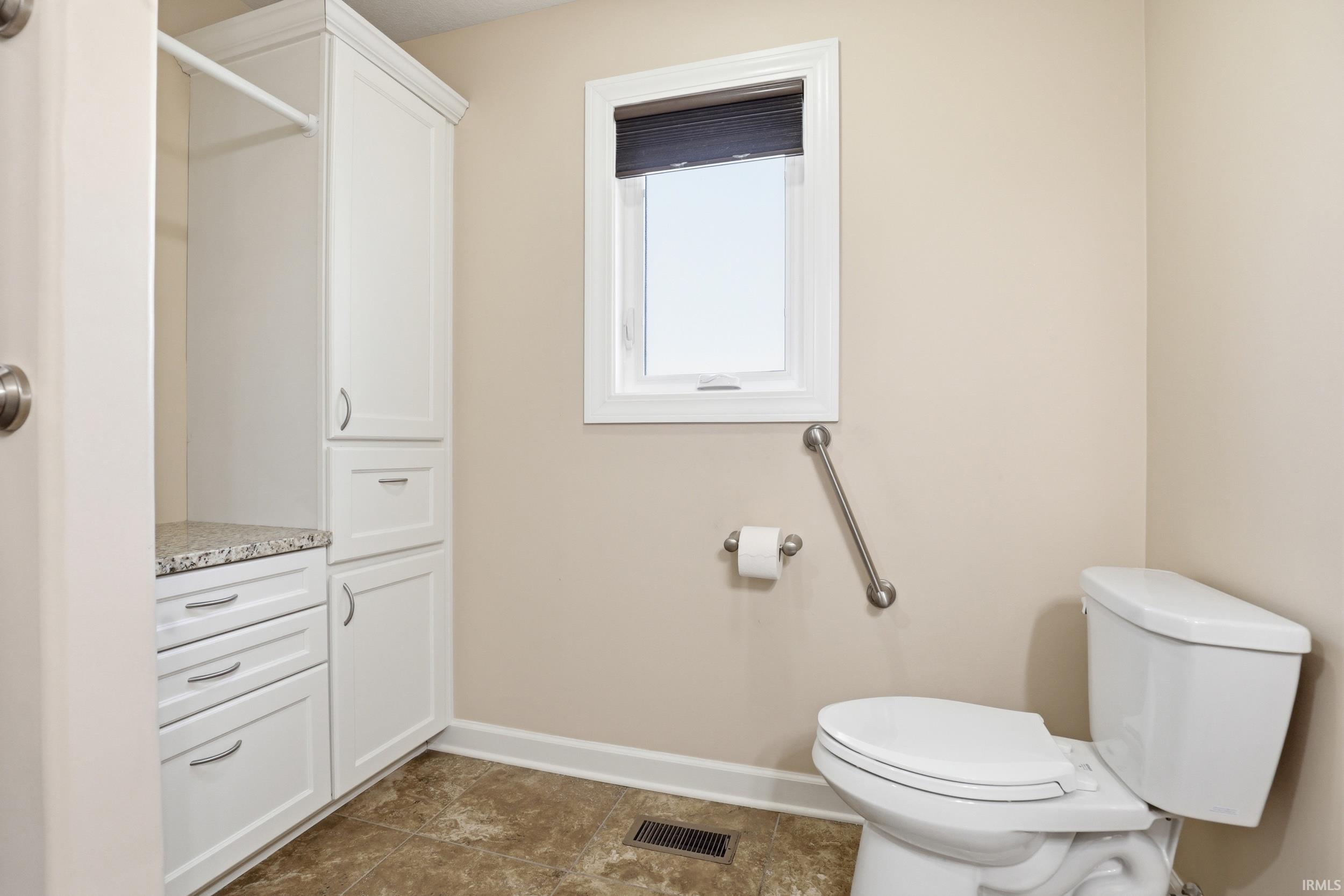 Bathroom featuring a white toilet, grab bar, and a window with a dark blind