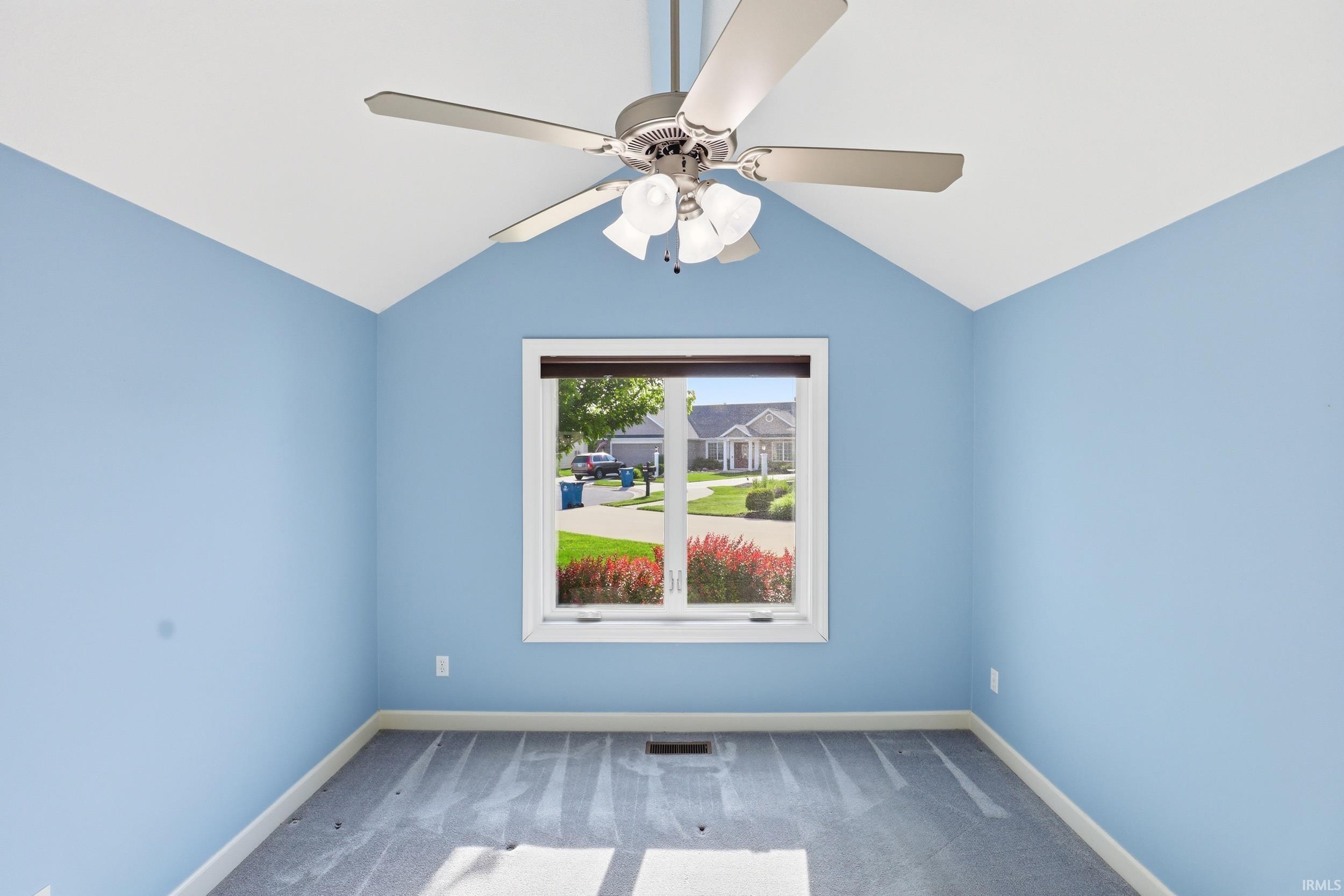 Vaulted ceiling room featuring a central window, light blue wall paint, gray carpeting, and a ceiling fan with integrated lighting