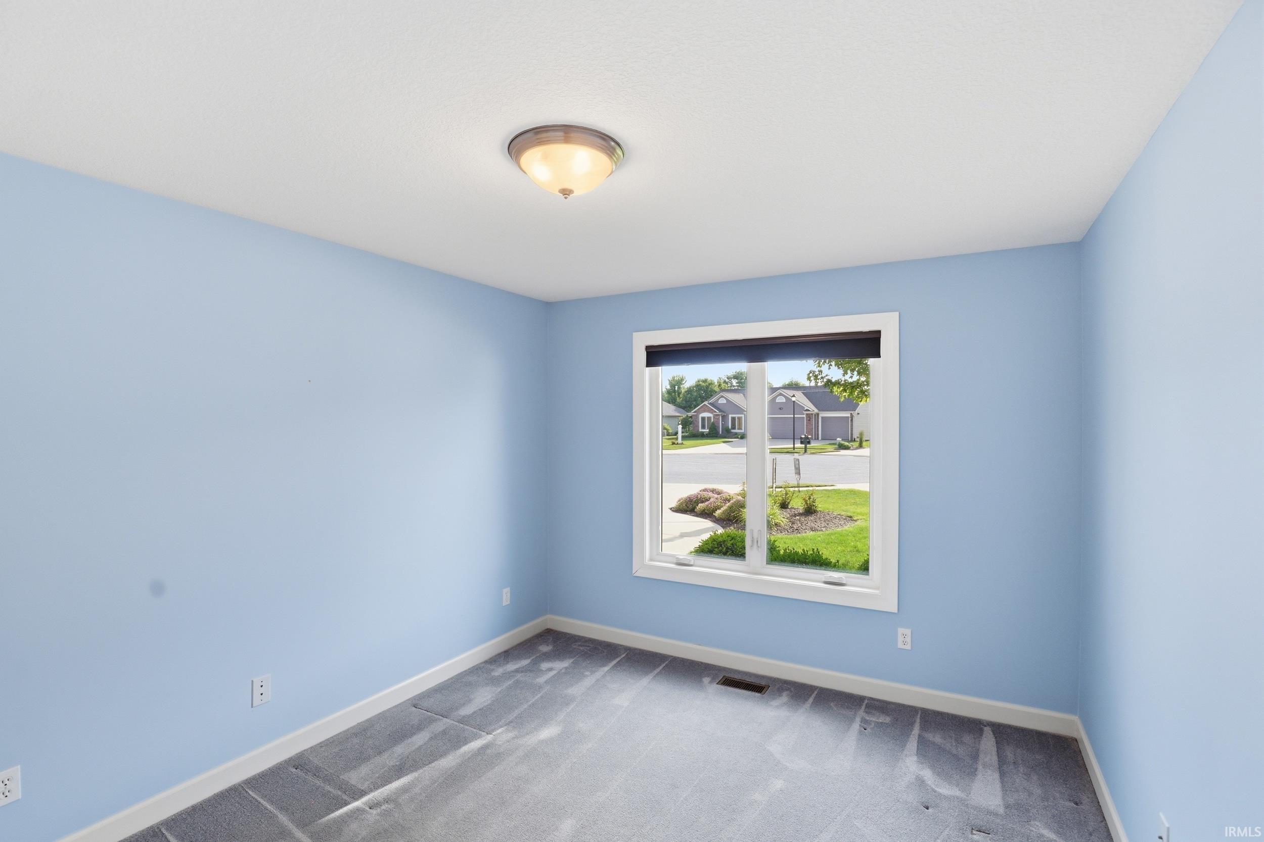 Light blue walls complementing gray carpeting, white trim, a single window, and a flush-mount ceiling light fixture