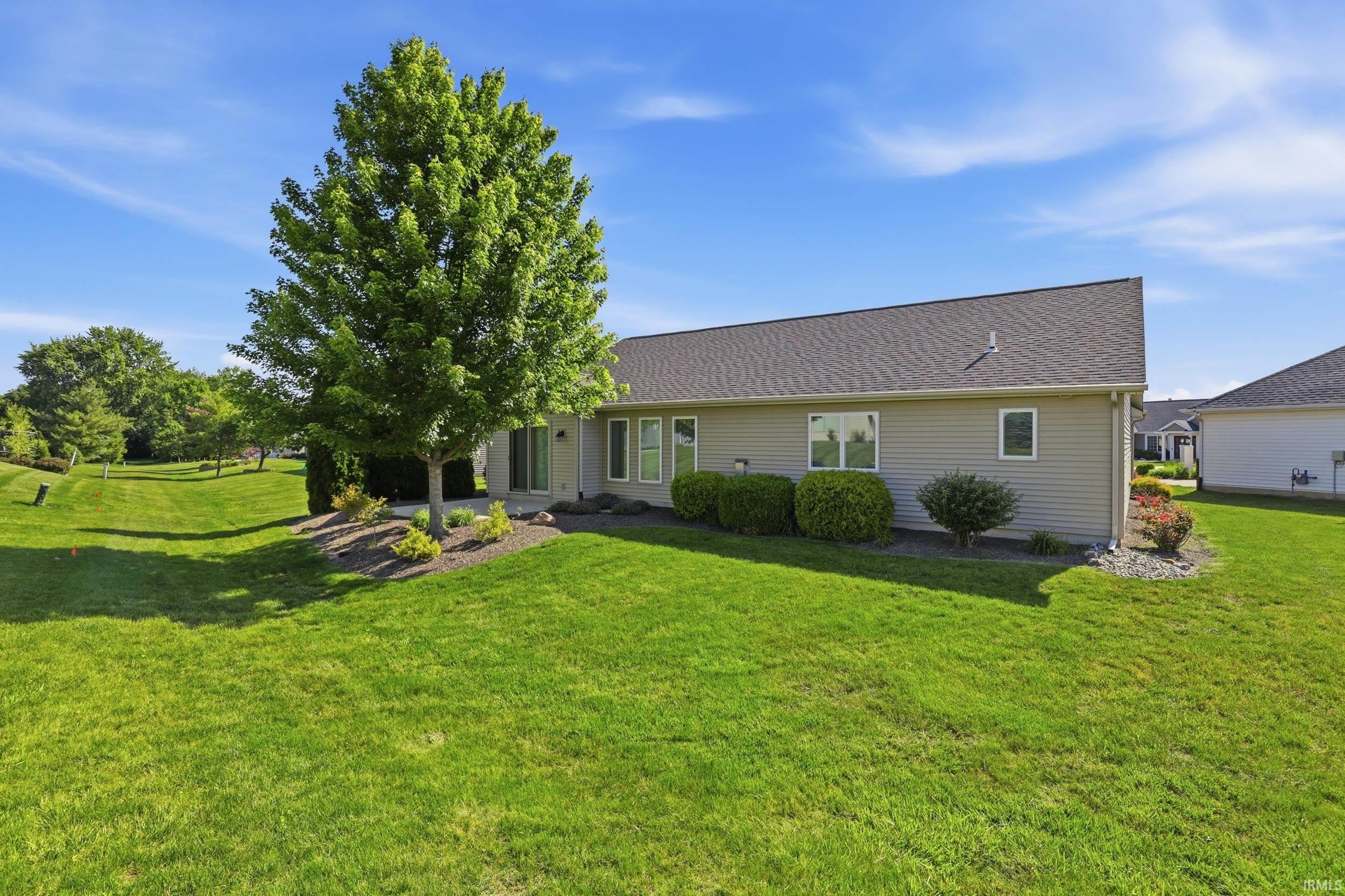 Expansive backyard featuring a large green lawn, mature tree, and planted landscaping