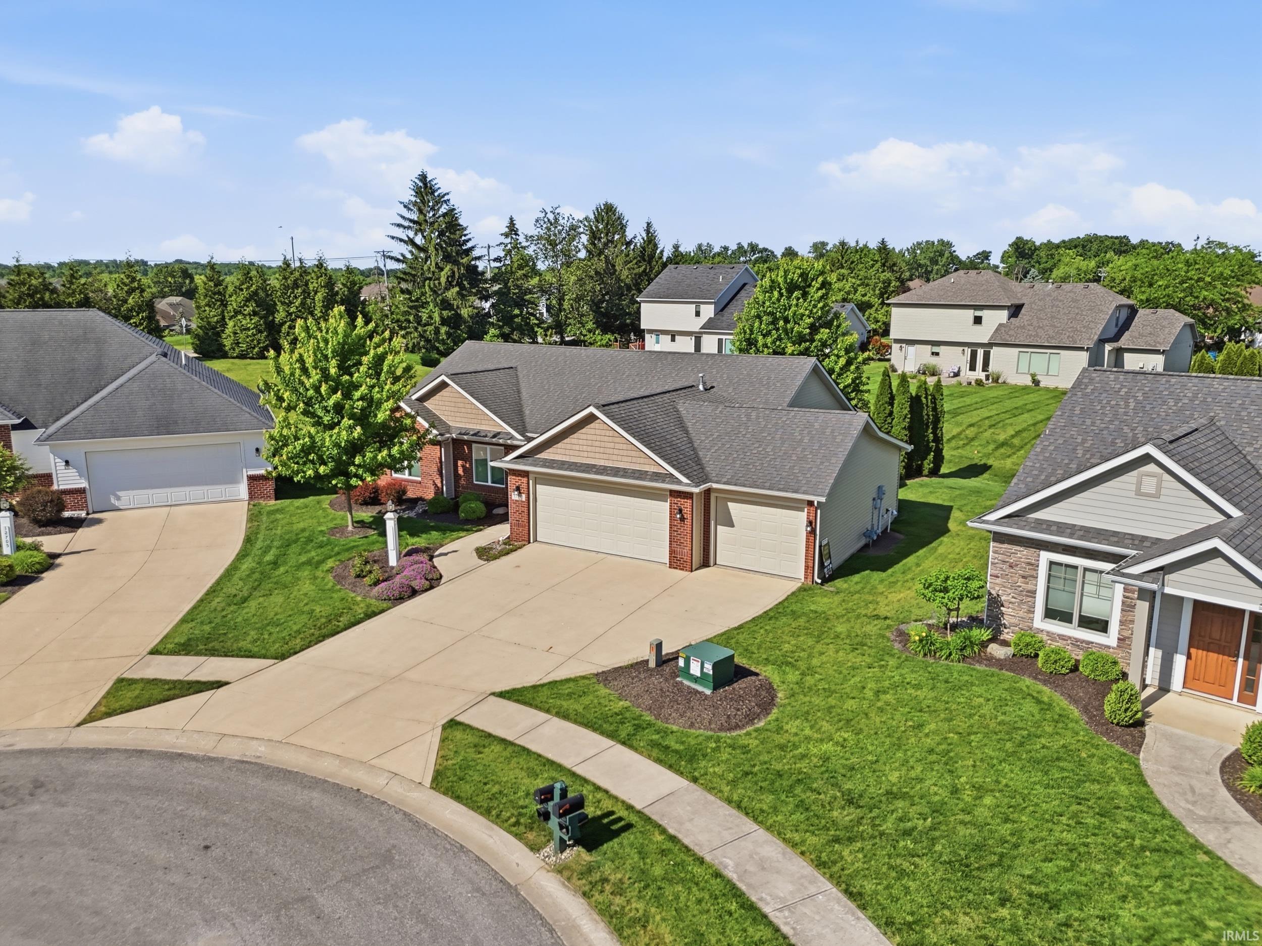 Residential property with brick and siding exterior, multi-car garage, concrete driveway, and established landscaping