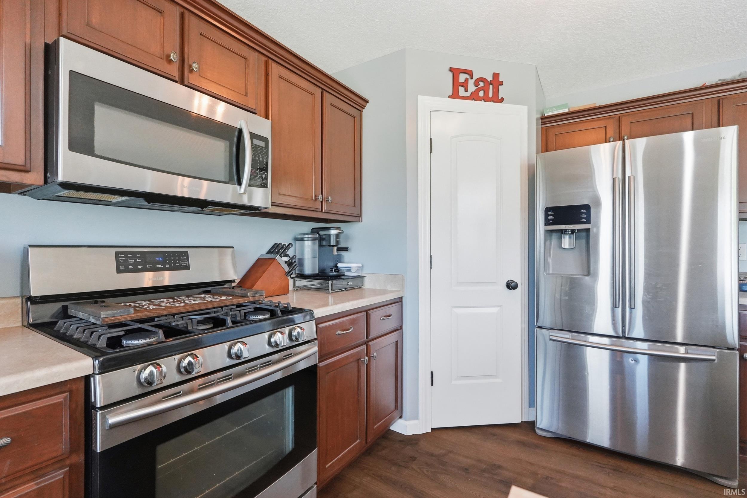 Kitchen featuring extensive wood cabinetry, stainless steel appliance suite including a French door refrigerator and gas range, light-toned countertops, and wood-finish flooring