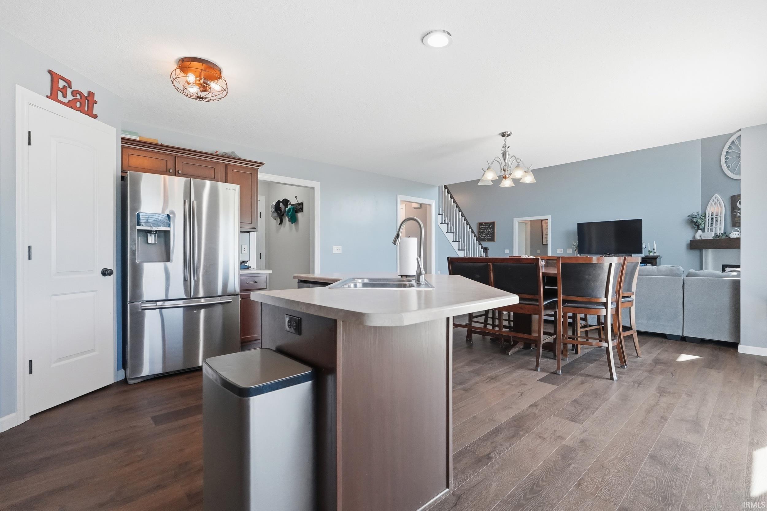 Kitchen island with an undermount sink and gooseneck faucet, stainless steel refrigerator, warm wood-finish flooring, and recessed ceiling lighting