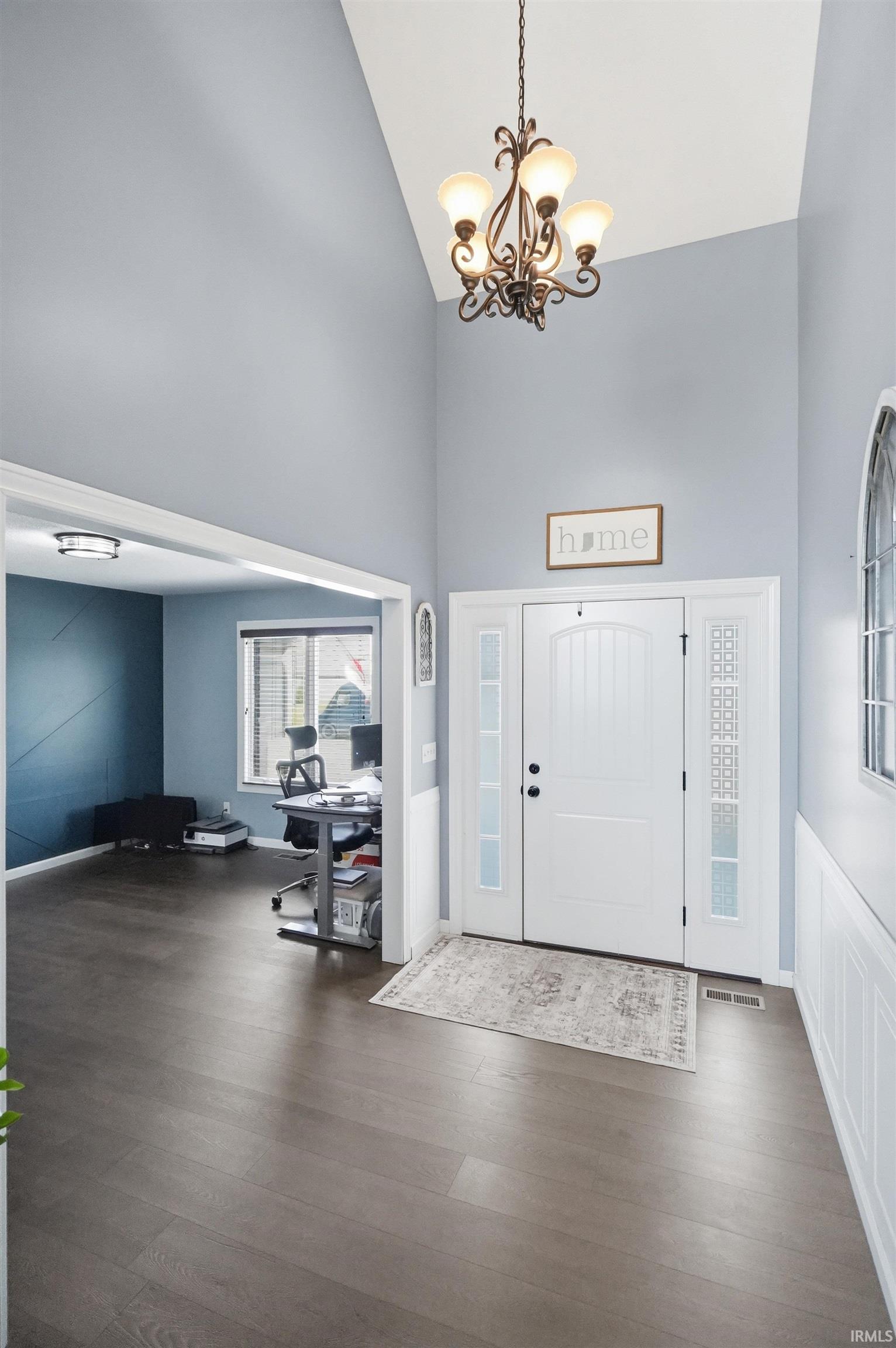 Soaring vaulted ceilings in the entryway featuring a decorative chandelier and wood-finish flooring