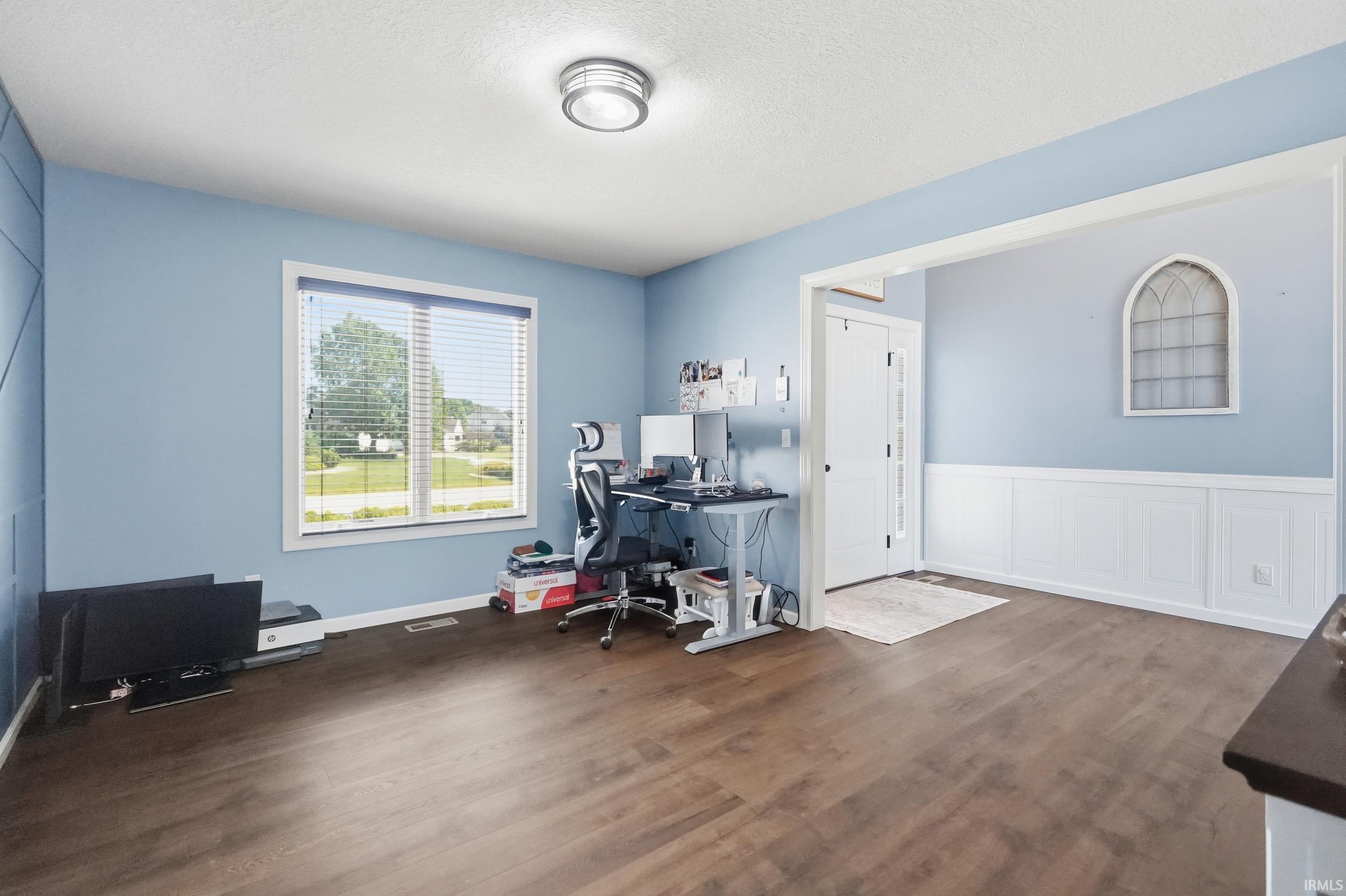 Spacious interior room featuring wood-finish flooring, a contemporary ceiling light fixture, and a large window with blinds