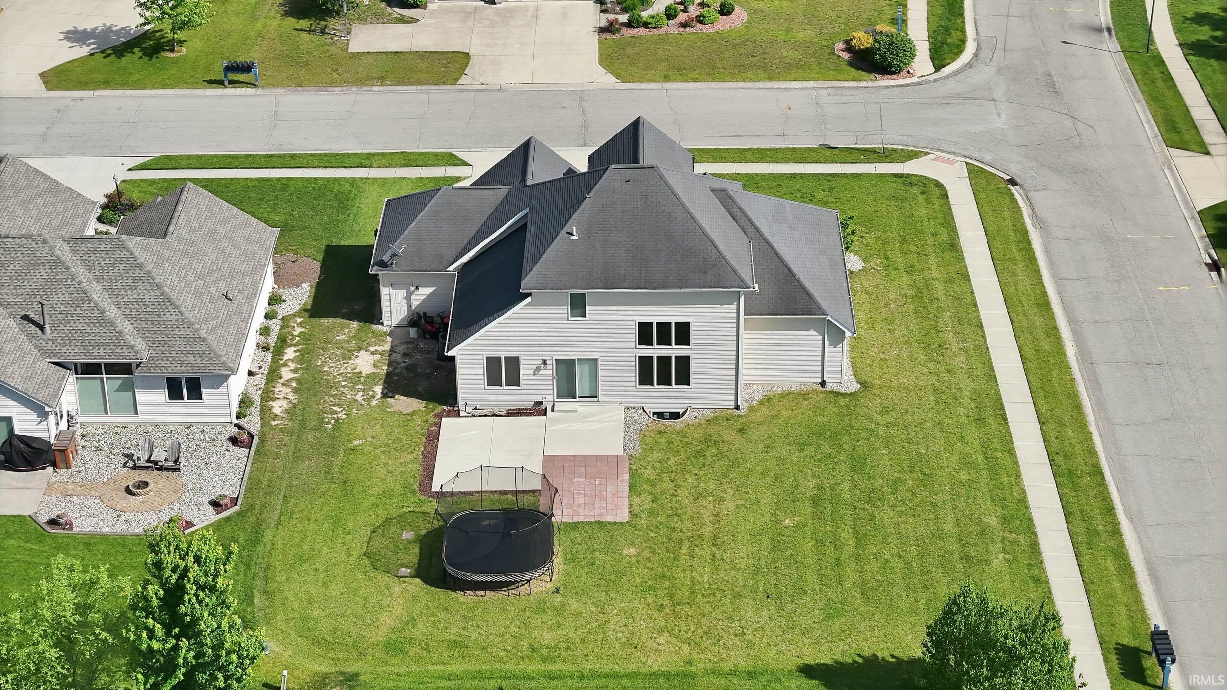 Expansive rear yard featuring a large patio area with concrete and paver sections, a sliding glass door for outdoor access, and multiple windows across the rear facade