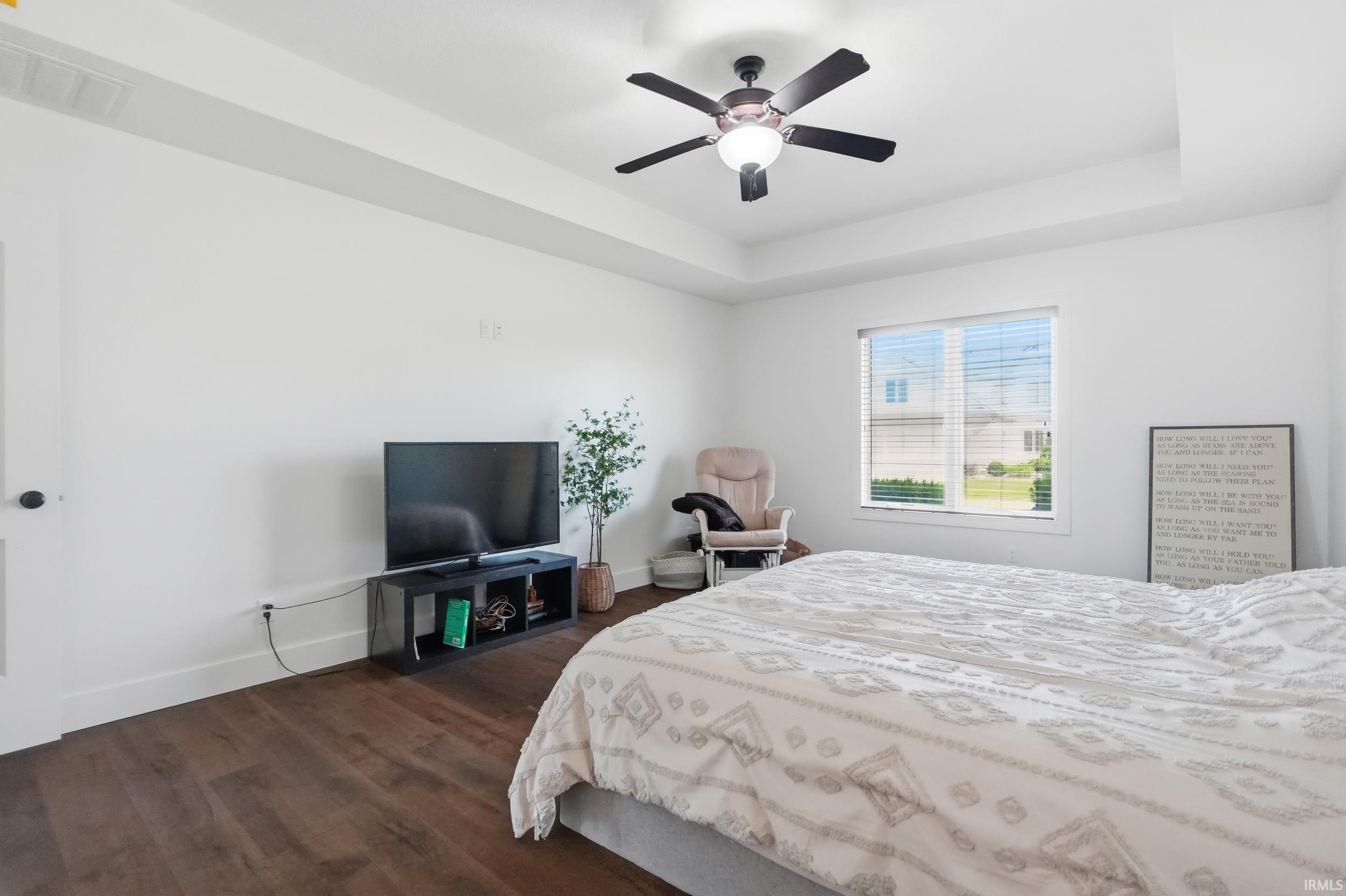 Spacious room featuring wood-finish flooring, a tray ceiling, and a ceiling fan with integrated lighting