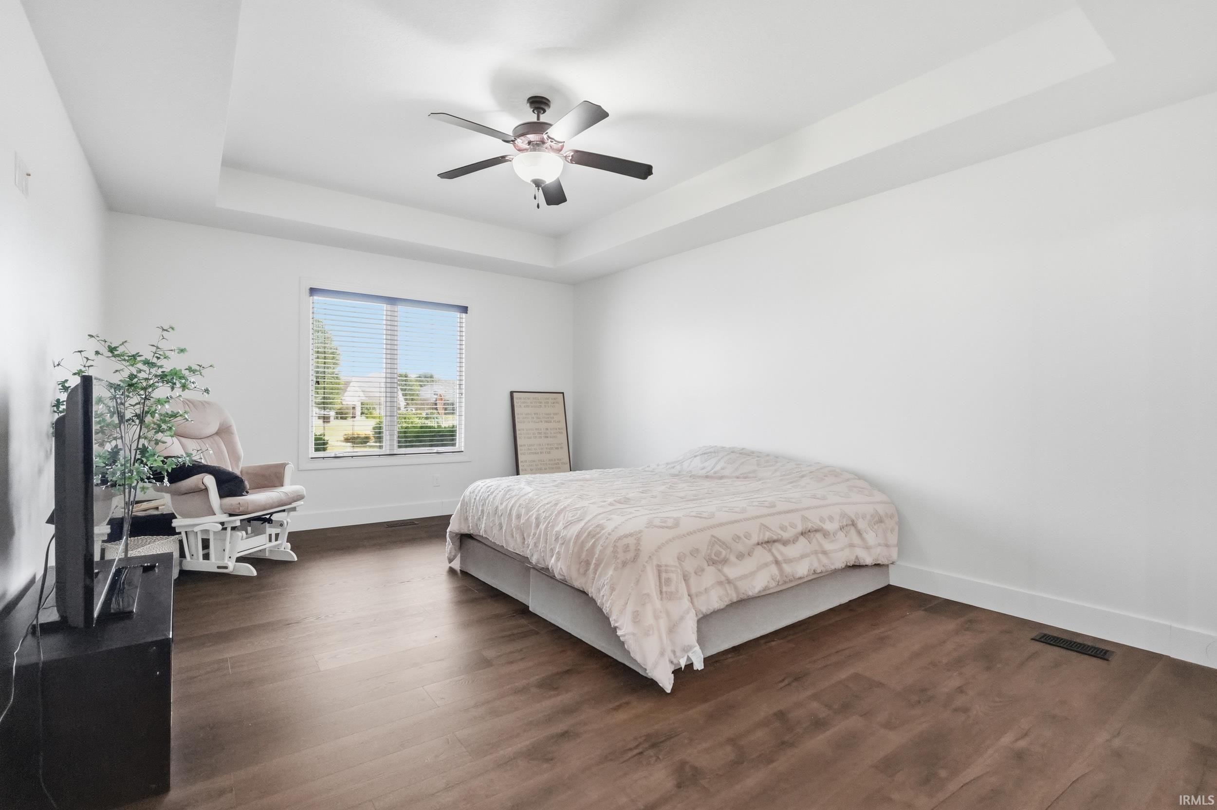 Spacious room featuring wood-finish flooring, a tray ceiling, and a ceiling fan with integrated lighting