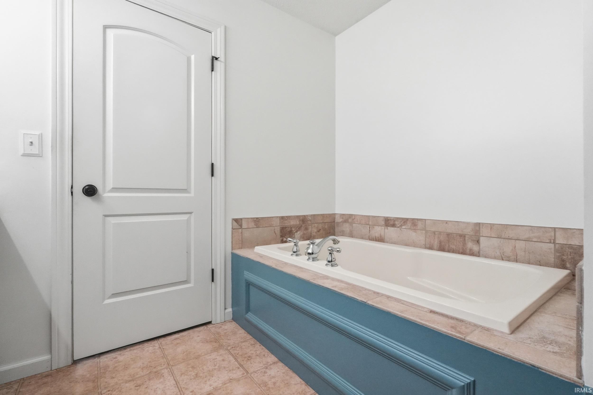 Built-in bathtub with a blue paneled surround, light-toned tile decking, and coordinating tile wainscoting