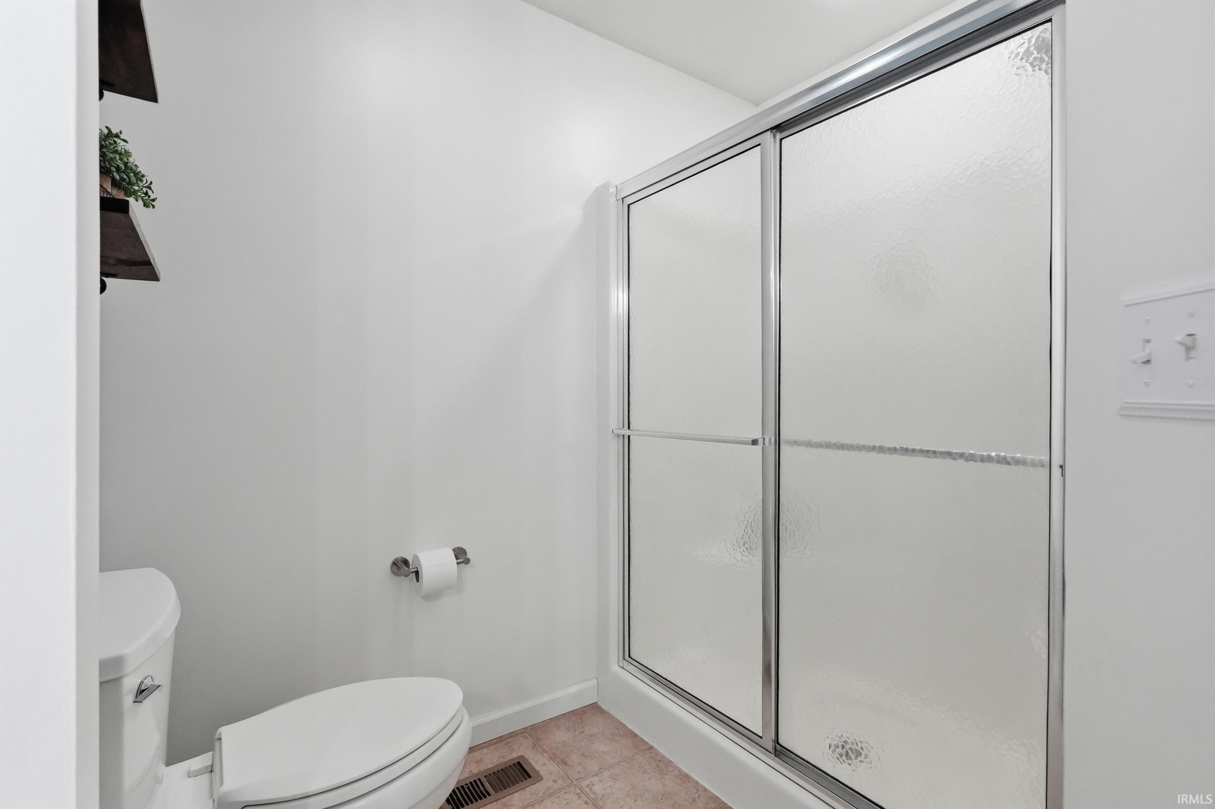 Shower enclosure with sliding frosted glass doors, white toilet, and wood-finish open shelving
