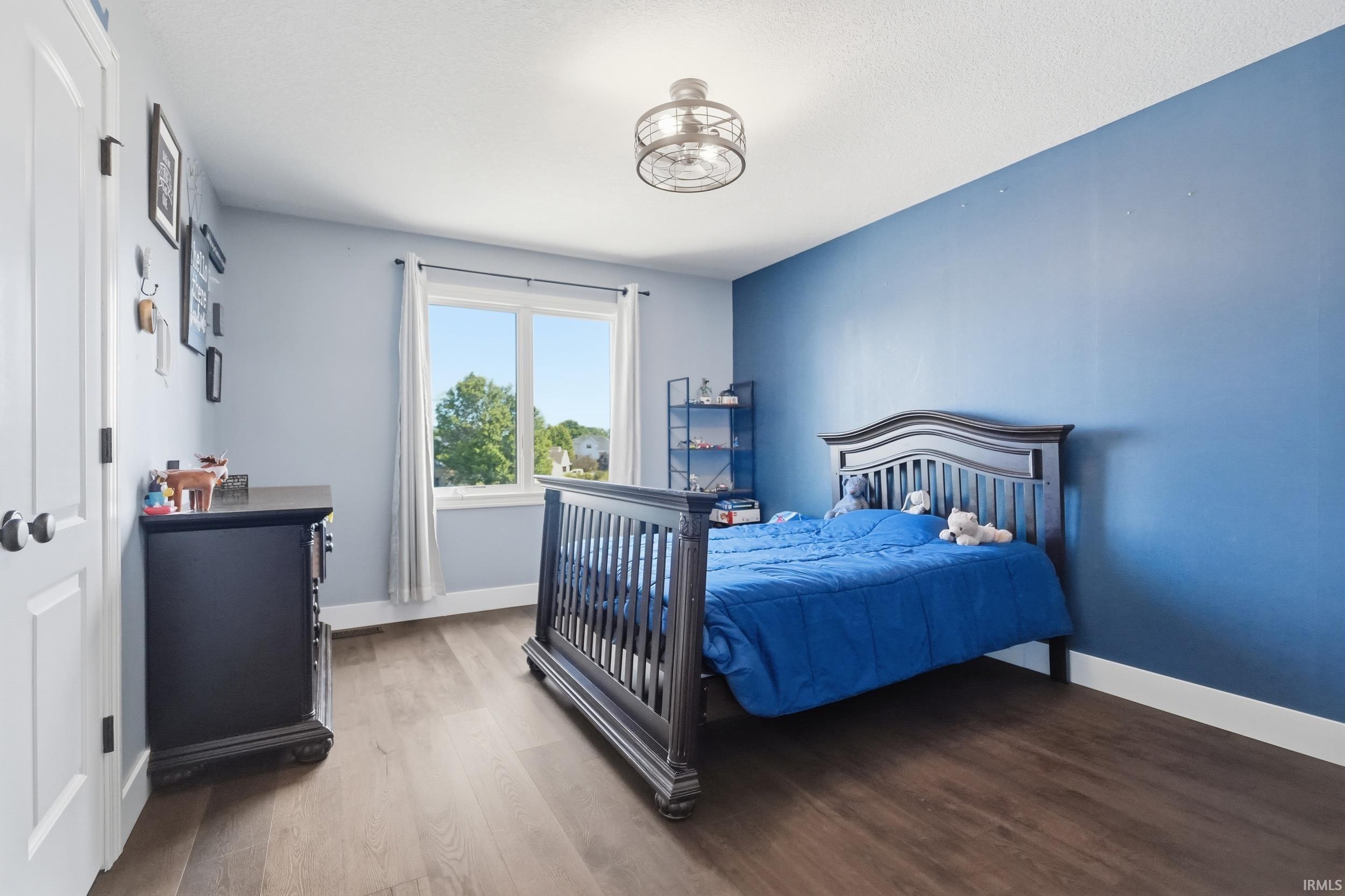 Spacious room featuring wood-finish flooring, a large window with white trim, and a contemporary ceiling fixture