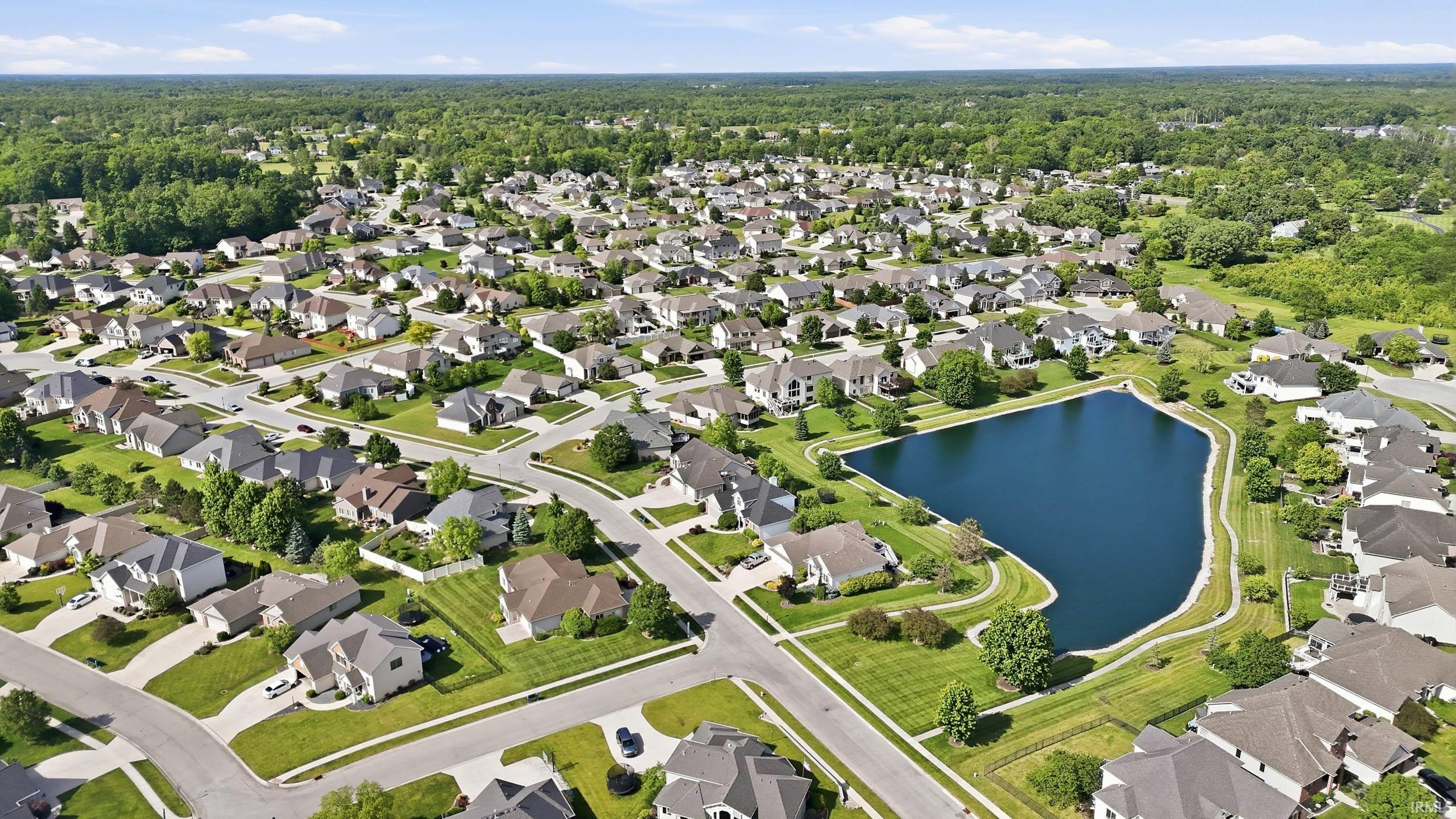 Aerial perspective of a developed residential community featuring a prominent central pond with surrounding green spaces