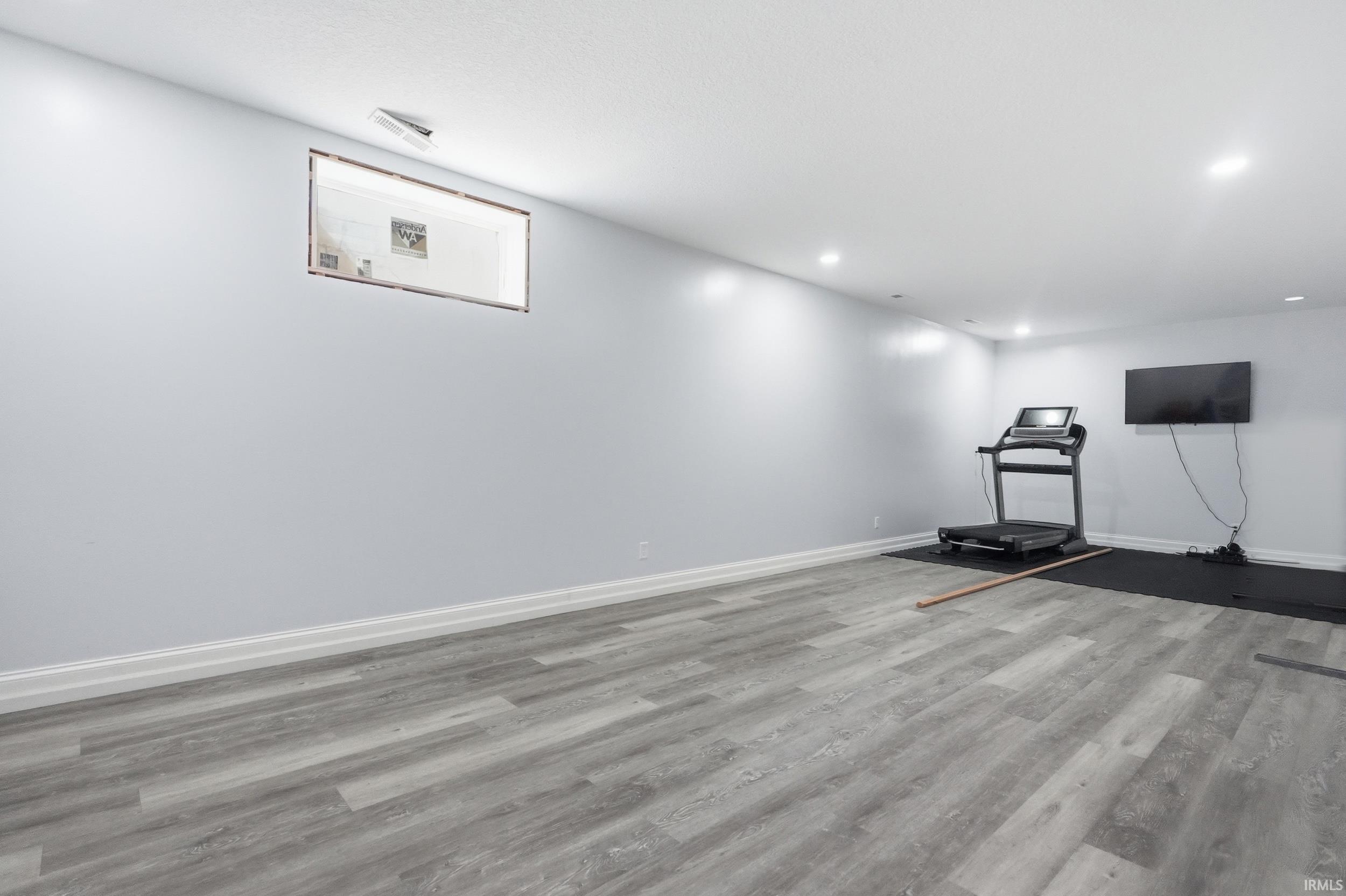 Spacious room featuring wood-finish flooring, light grey painted walls, white trim, recessed lighting, and a high window