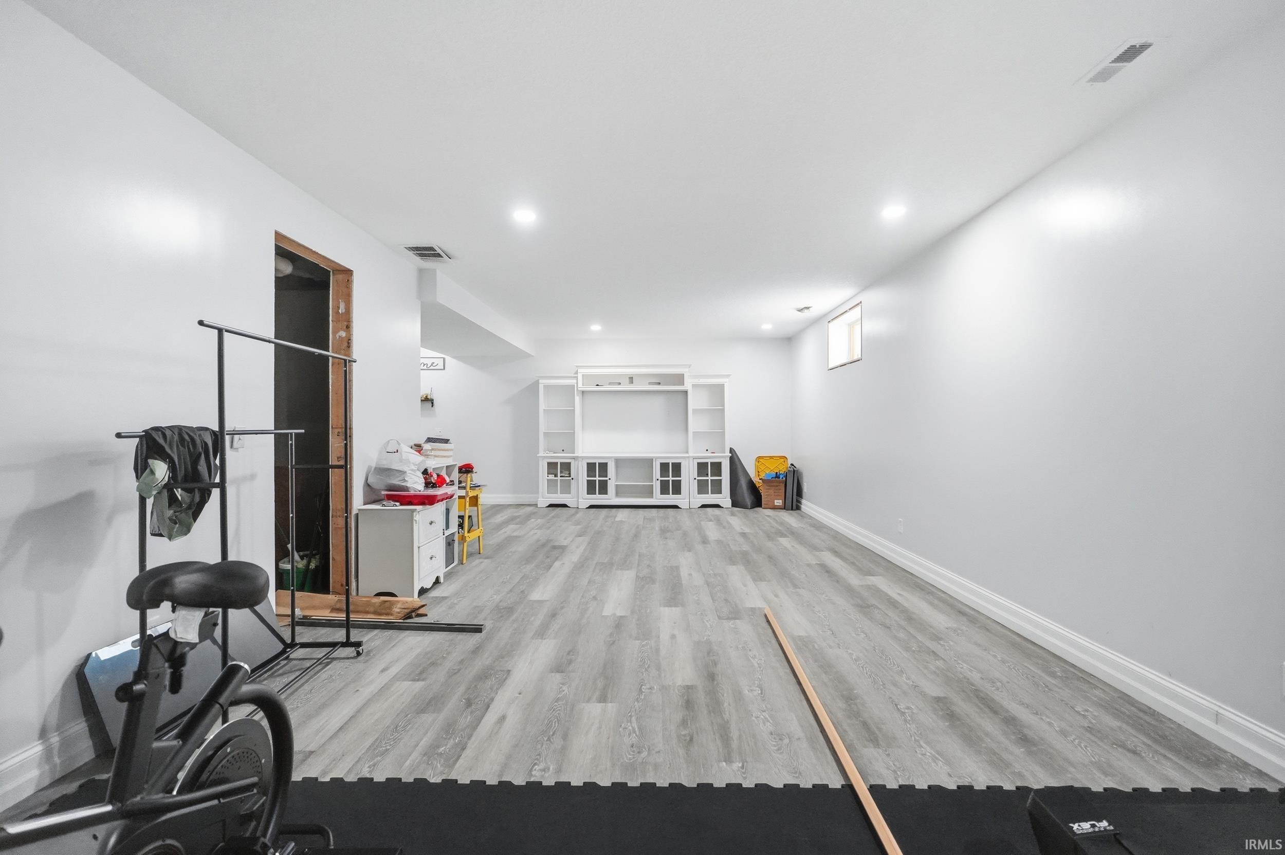 Spacious room featuring light gray wood-finish flooring, recessed lighting, white walls, and a built-in white media console with shelving