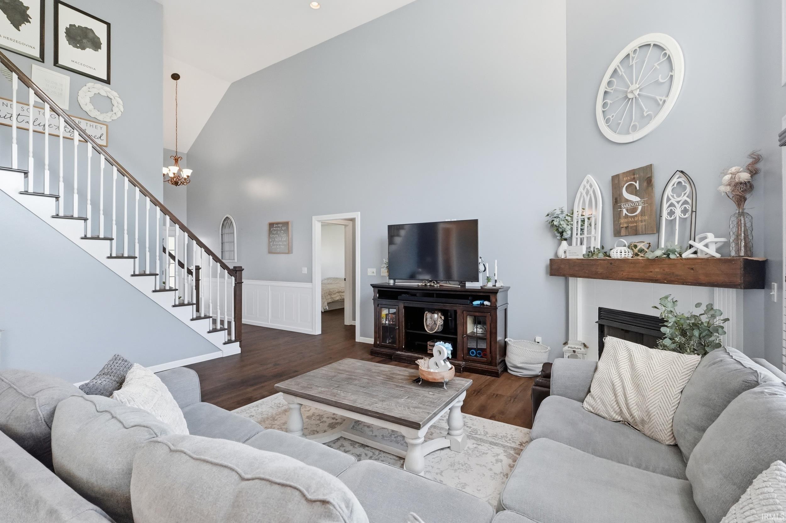 Vaulted ceiling living room featuring wood-finish flooring, a white spindle staircase with dark wood handrail, and a built-in fireplace with a substantial wood mantel