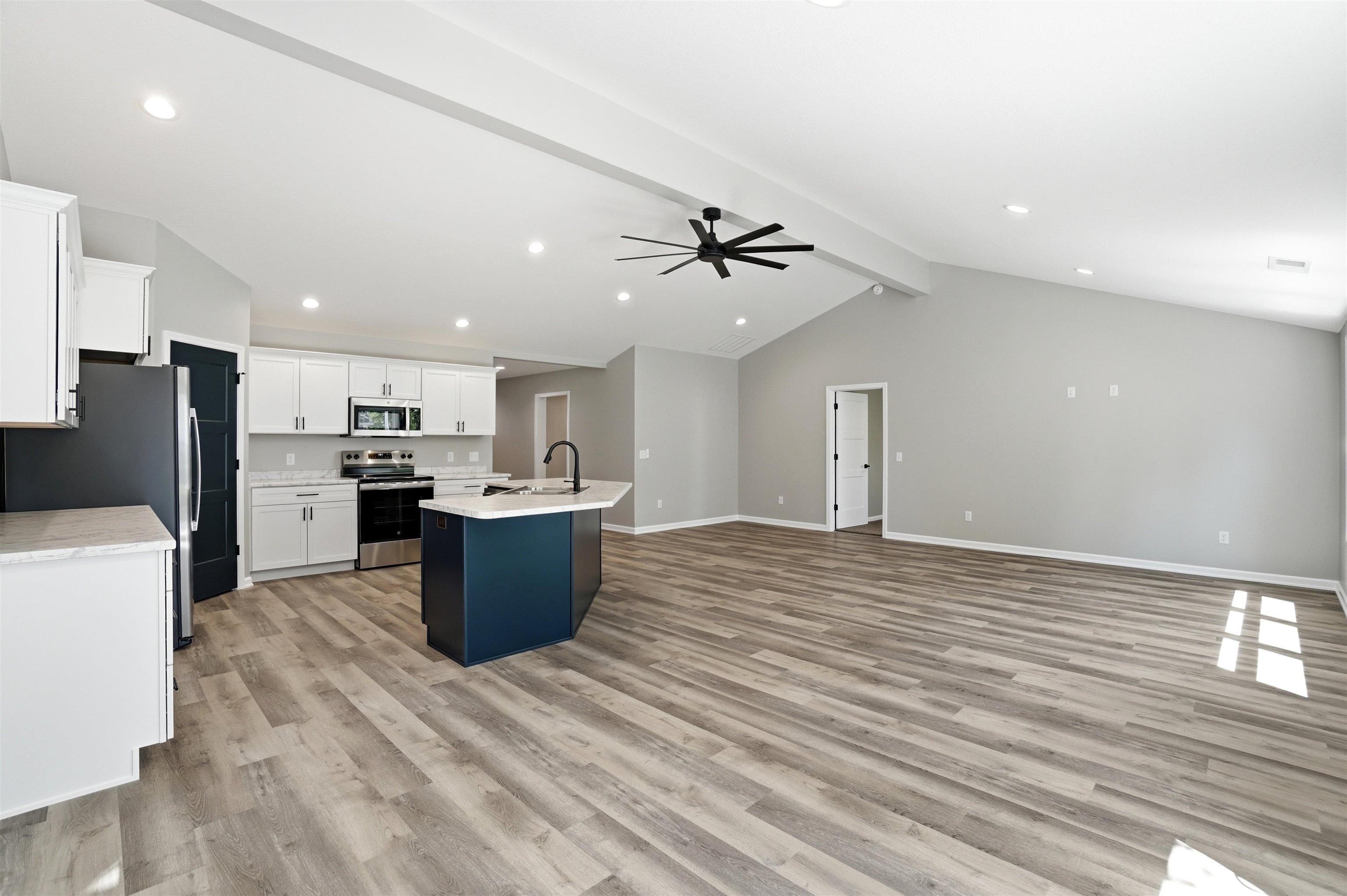 Open-concept living space featuring a vaulted ceiling with exposed beam, wood-finish flooring, recessed lighting, and a modern ceiling fan
