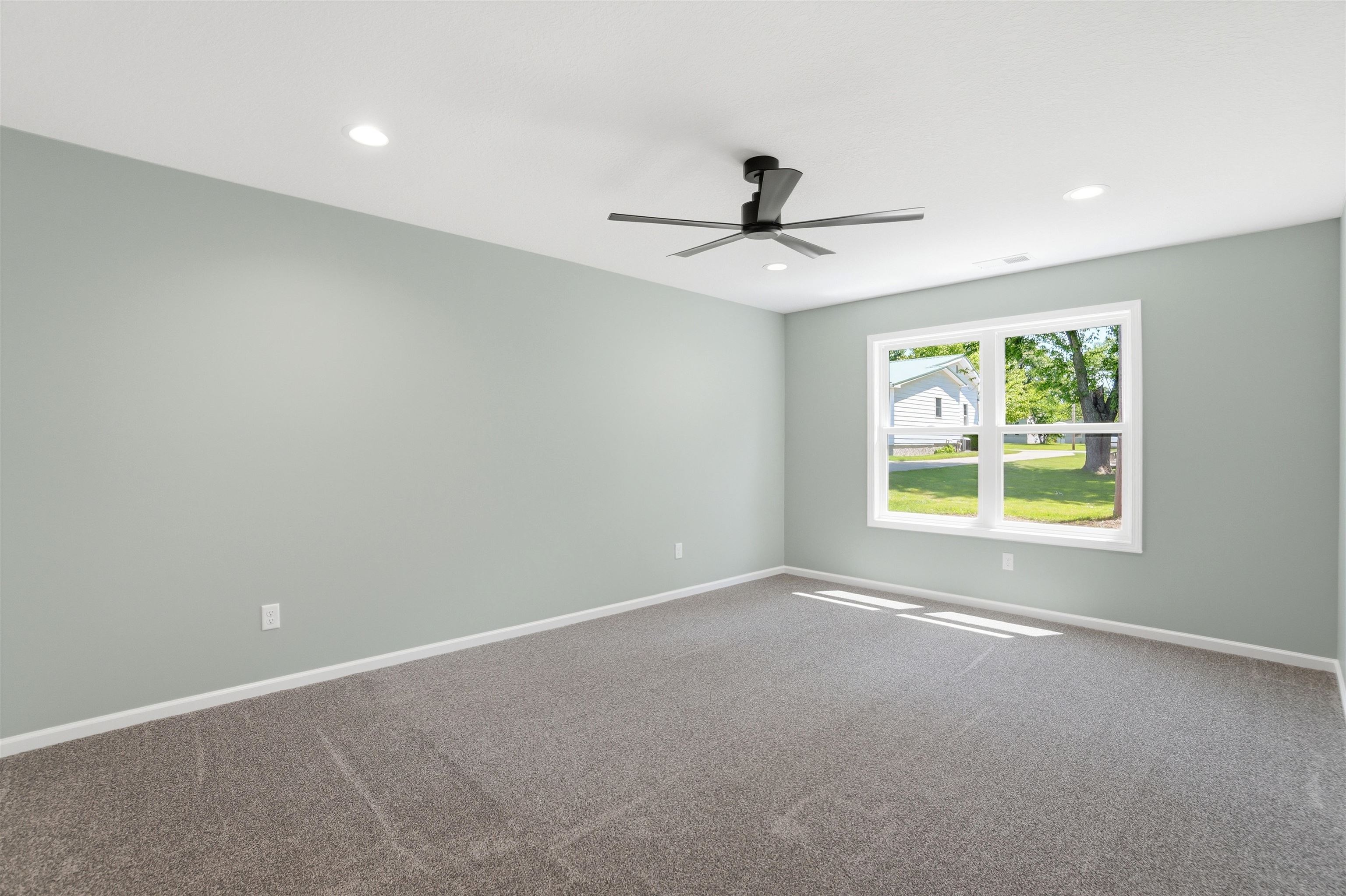 Spacious room featuring neutral carpeting, light-toned walls, and a modern ceiling fan