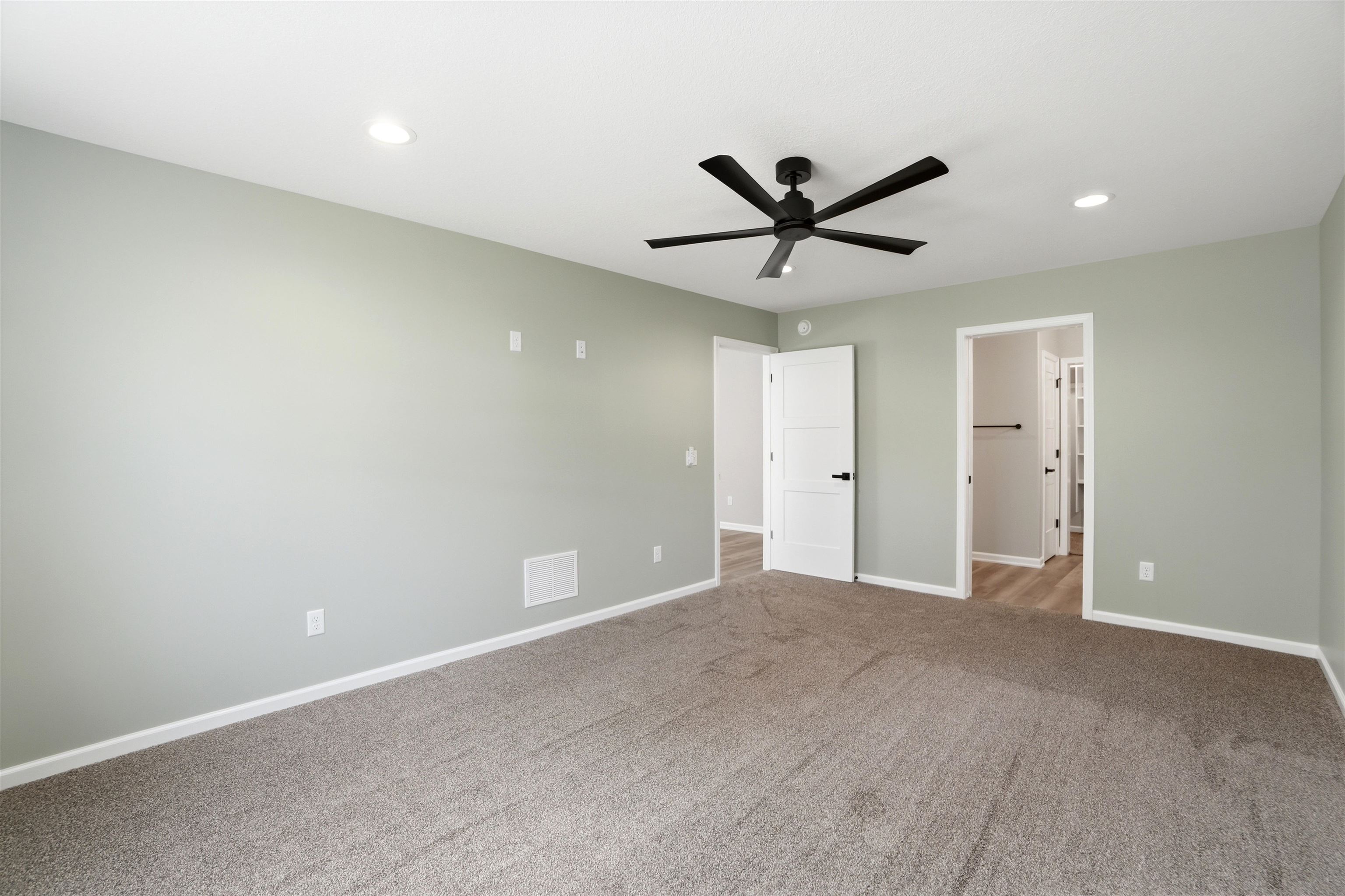 Spacious interior room featuring light-colored walls, carpet flooring, a modern black ceiling fan, and recessed lighting