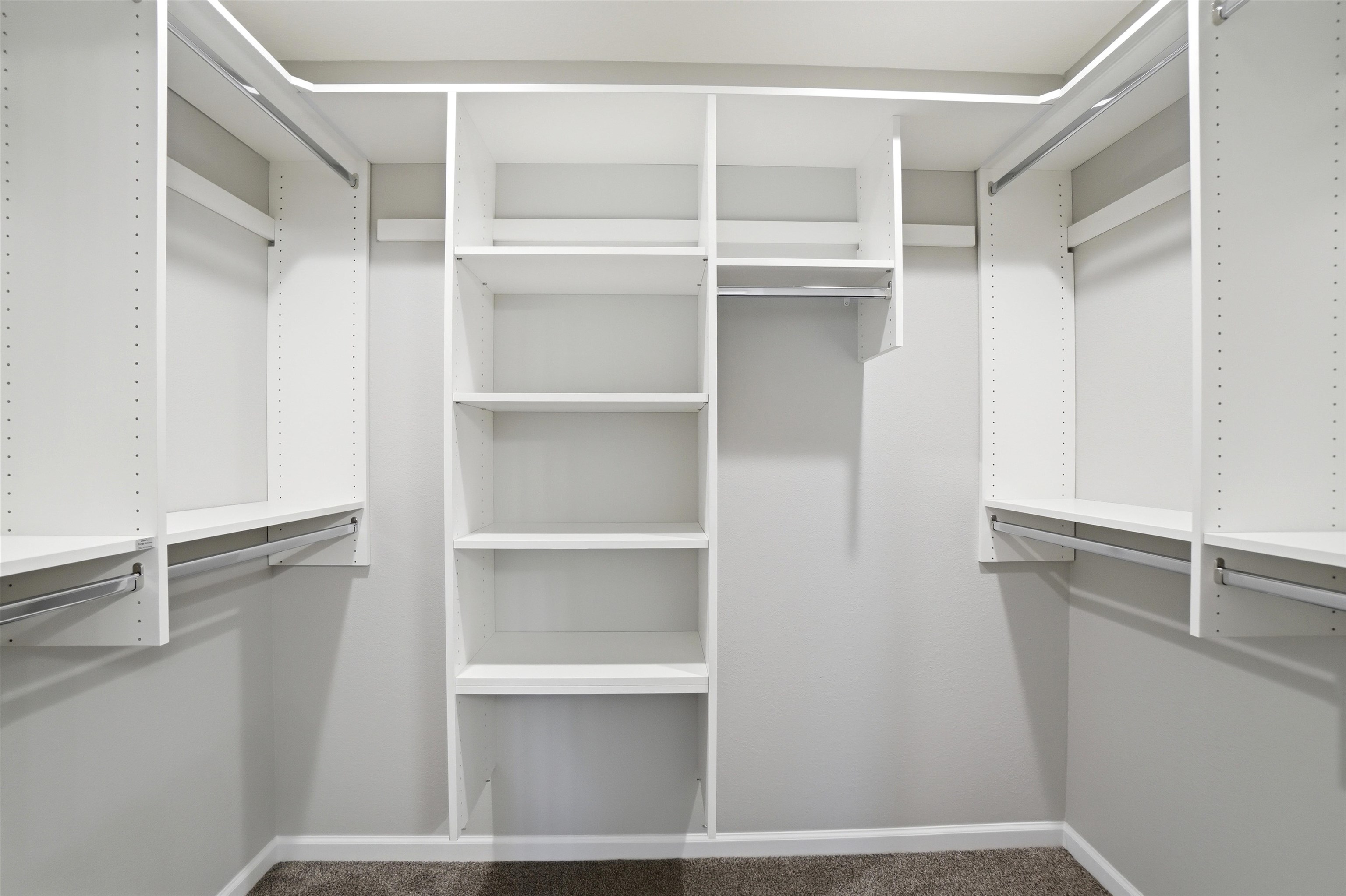 Walk-in closet featuring white built-in shelving, multiple hanging rods, and carpet flooring