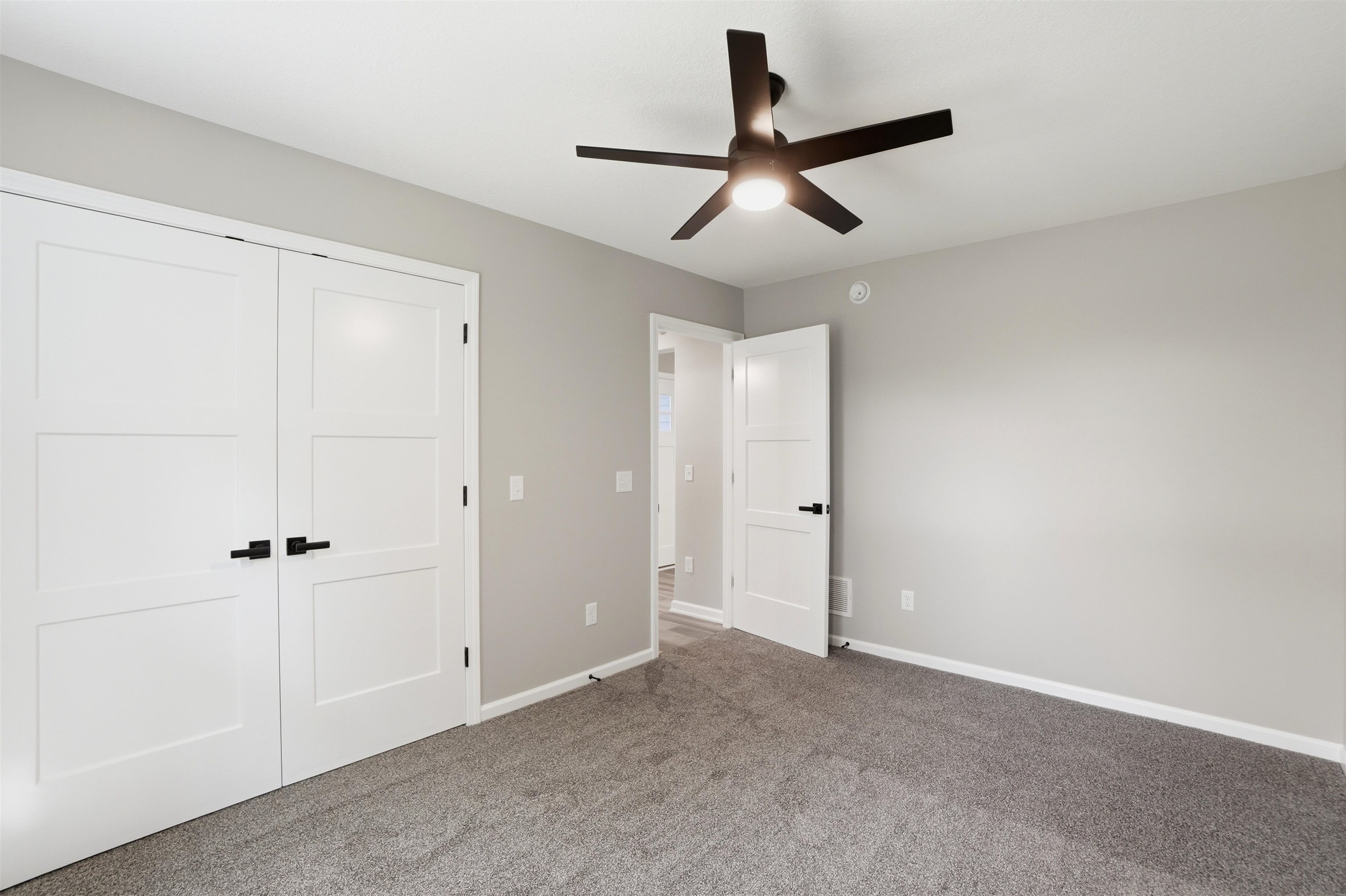 Room featuring light gray wall paint, gray carpet flooring, and a ceiling fan with matte black blades and integrated lighting