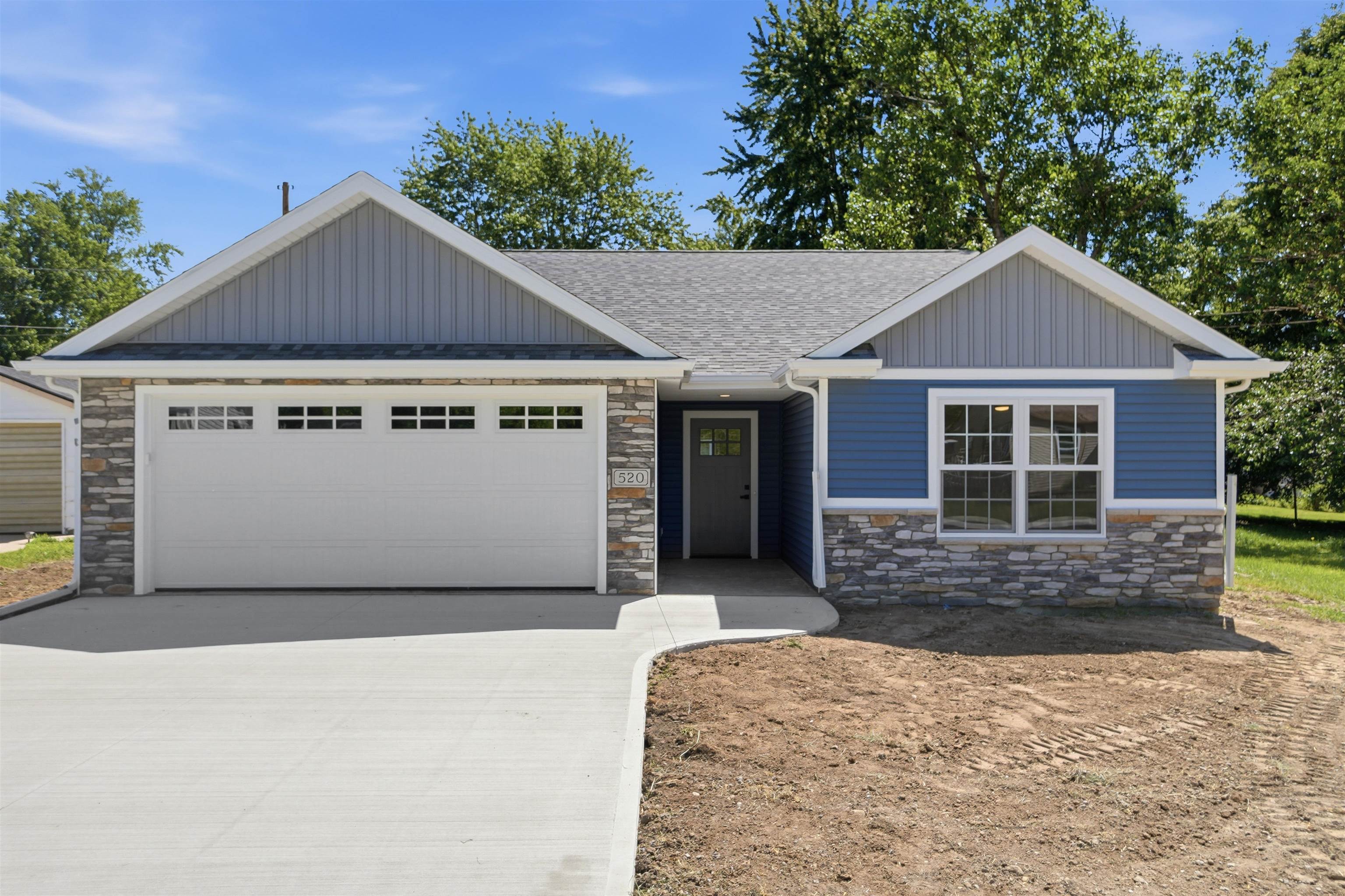 Contemporary home exterior featuring blue siding, stone veneer accents, an attached two-car garage with transom windows, and a paved driveway