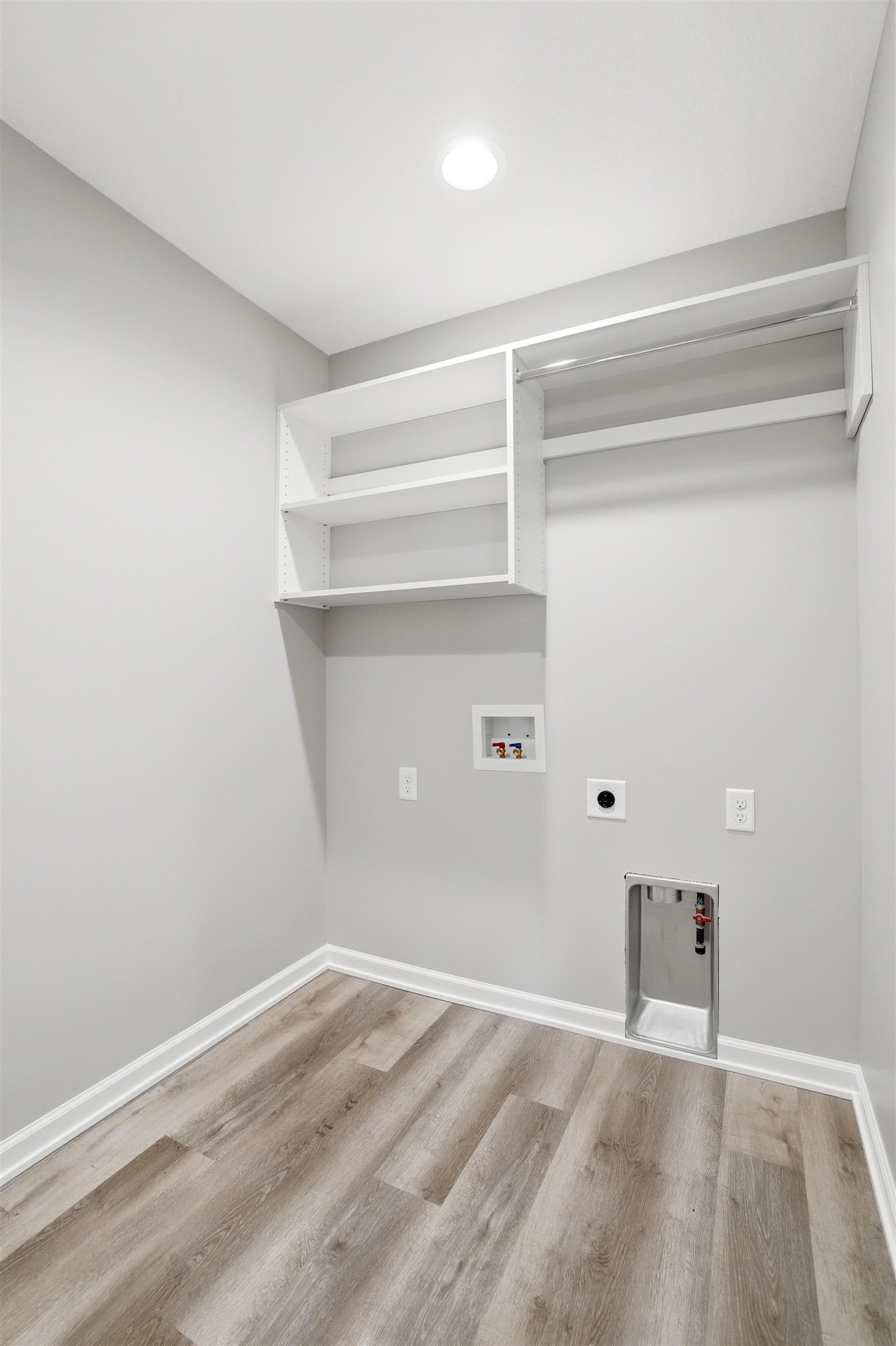 Laundry room featuring wood-finish flooring, light gray walls, built-in shelving, a clothes hanging rod, and recessed ceiling lighting