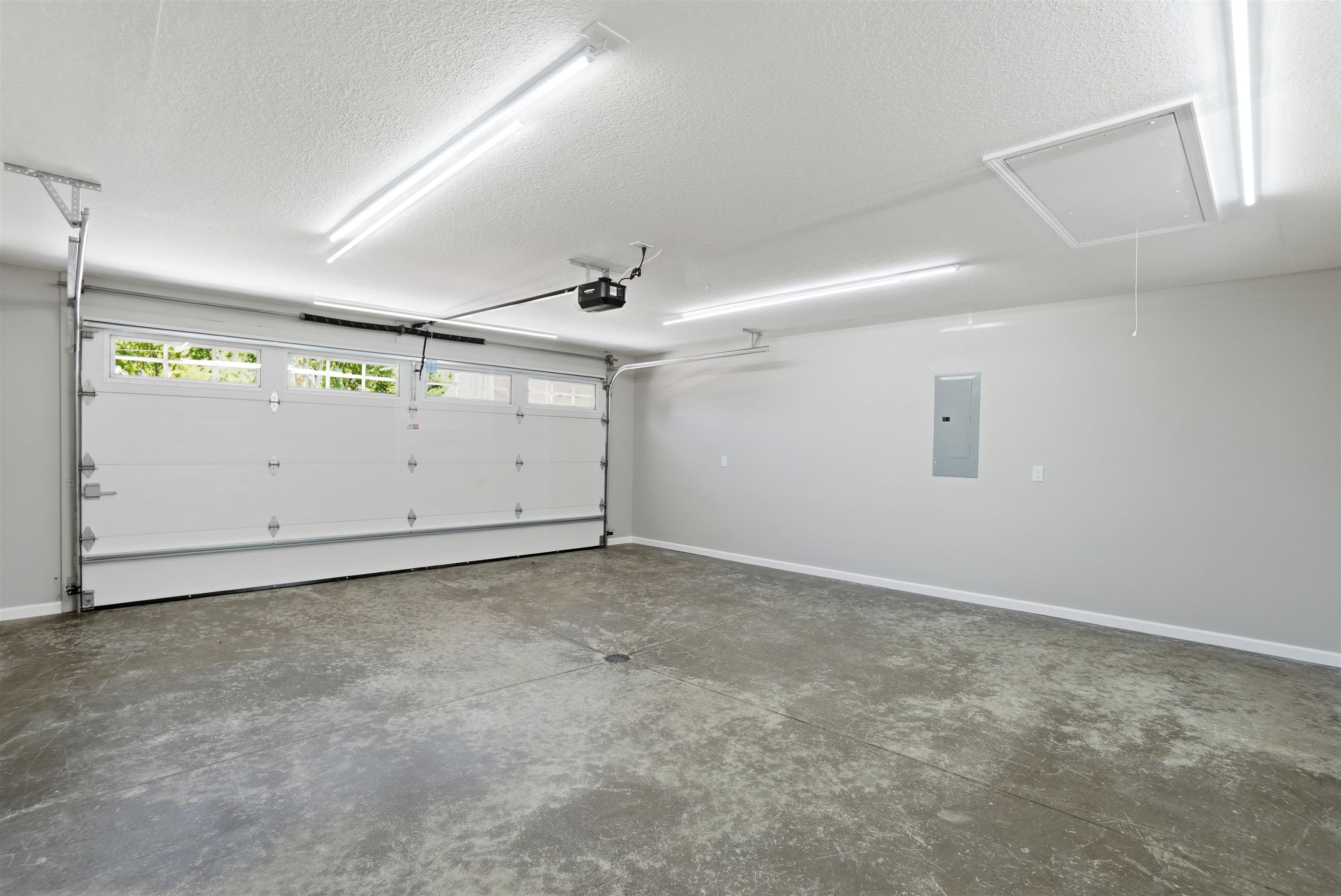 Spacious garage featuring a sectional overhead door with windows, concrete flooring, overhead fluorescent lighting, an automatic opener, and a ceiling access panel