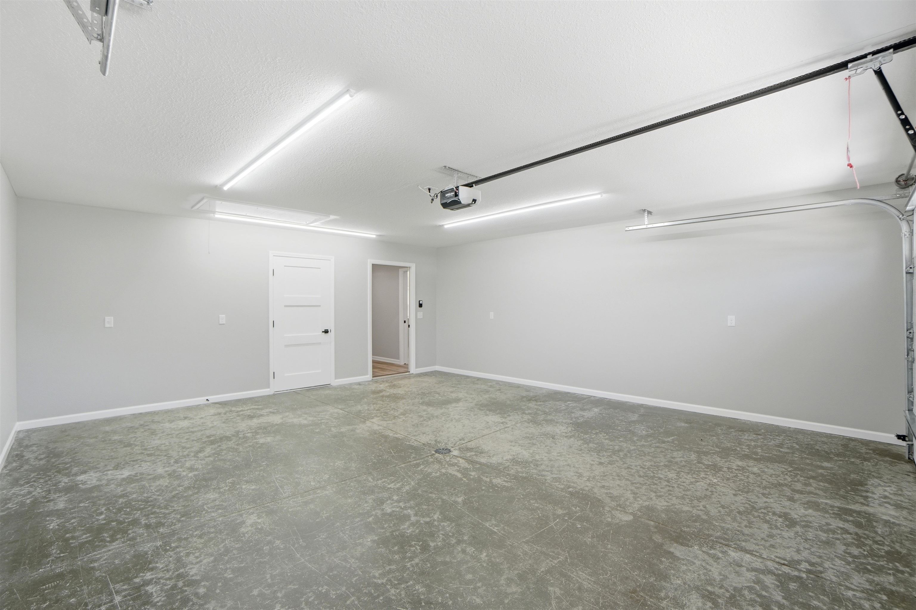 Spacious garage with light grey walls, concrete flooring, and multiple ceiling-mounted light fixtures