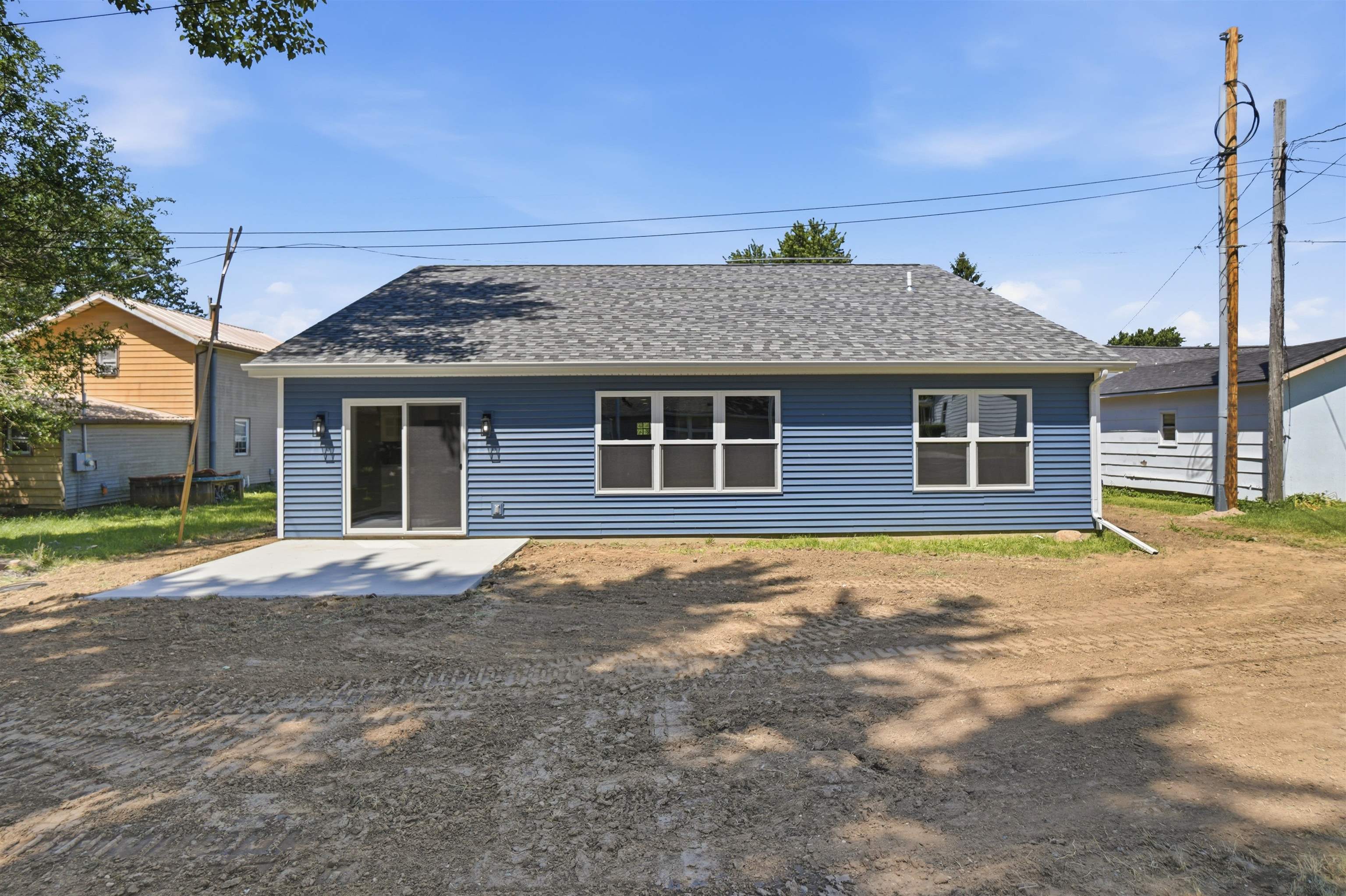 Rear exterior featuring blue horizontal siding, a gray shingle roof, and a concrete patio