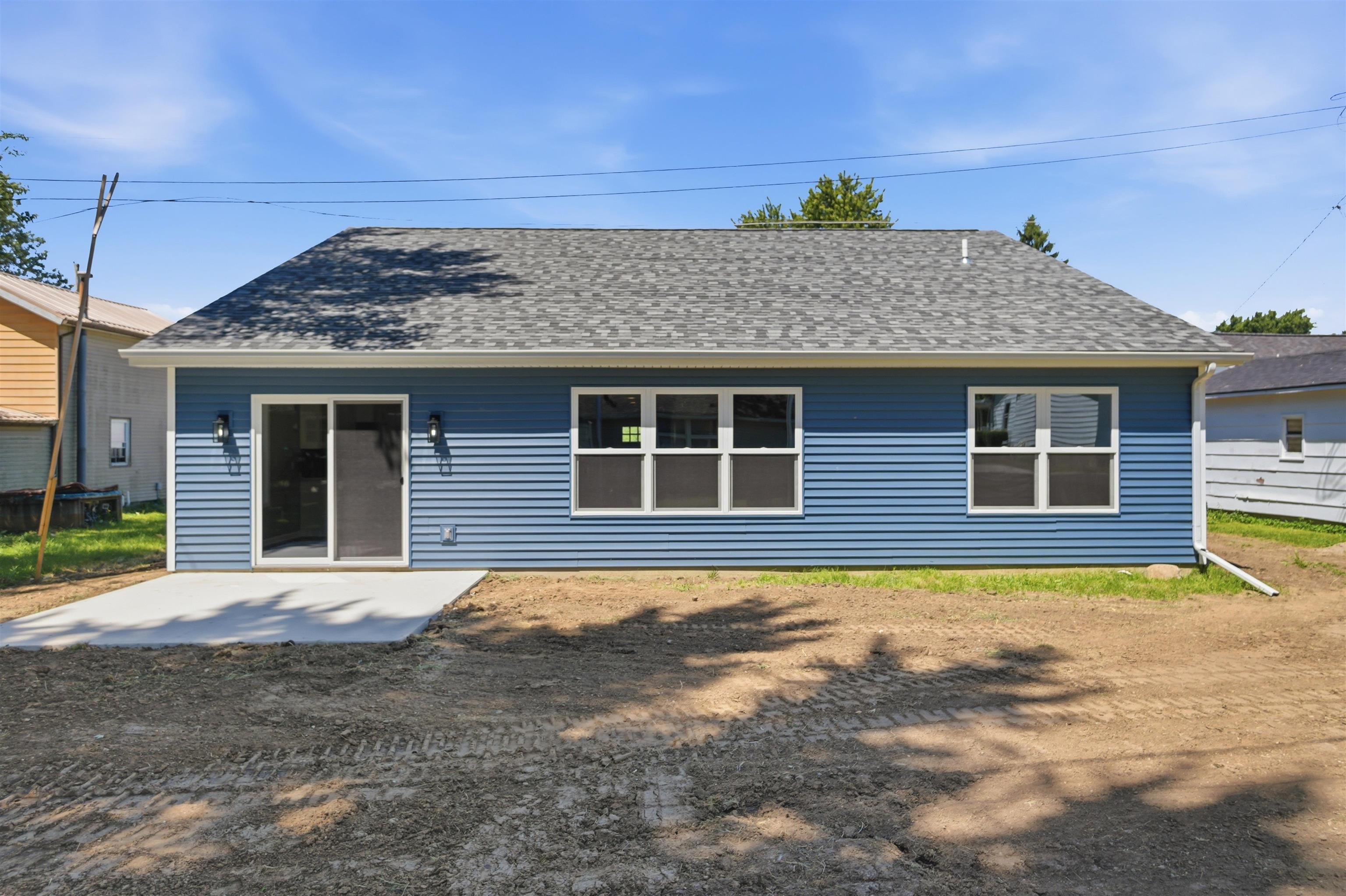 Rear exterior featuring blue horizontal siding, a gray shingle roof, and a concrete patio