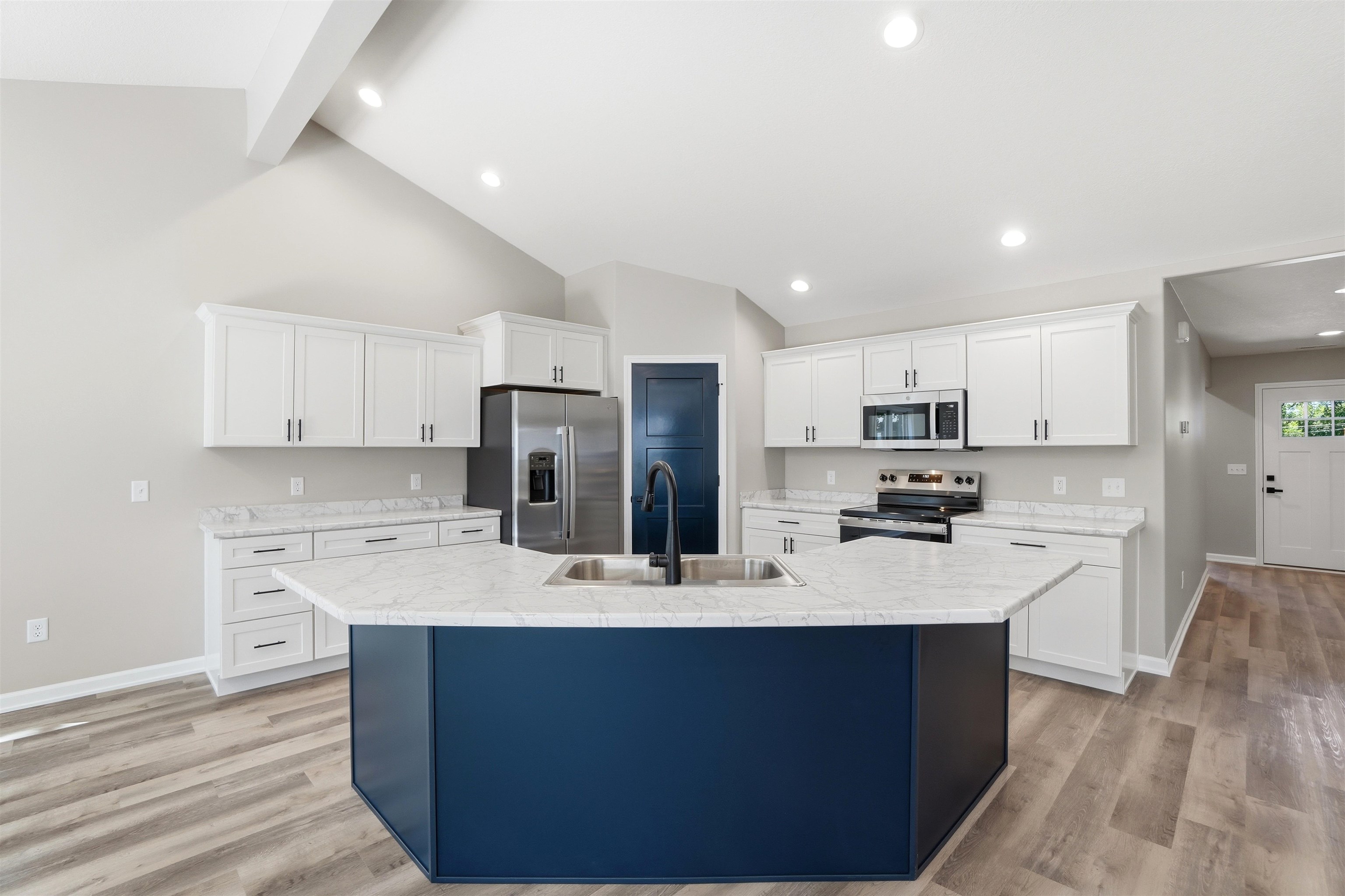 Open-concept kitchen featuring a bold blue island with integrated sink, white cabinetry, stainless steel appliances, and light-toned wood-finish flooring