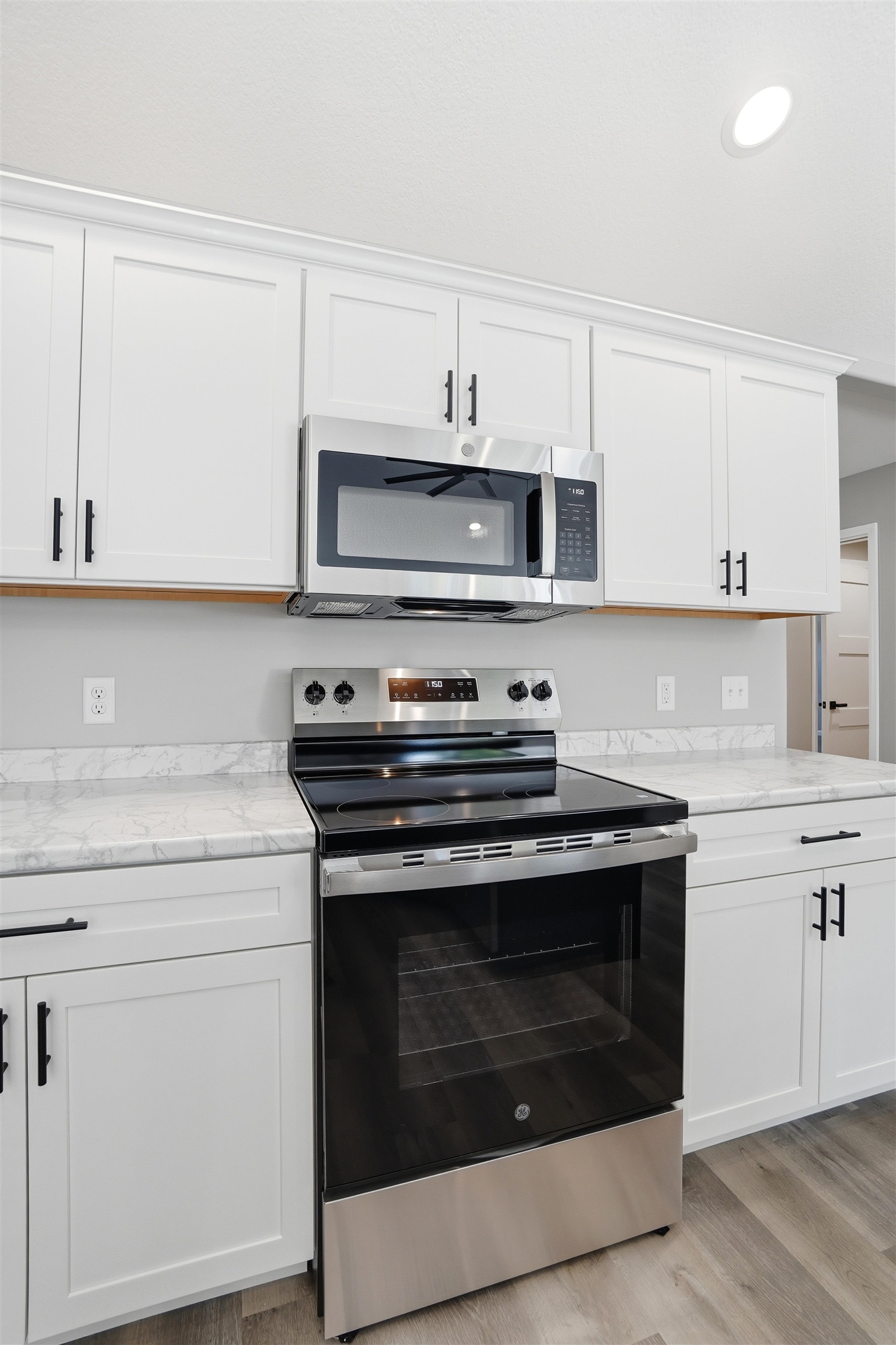 Kitchen featuring white shaker cabinetry, stainless steel appliances, stone-finish countertops, and wood-finish flooring