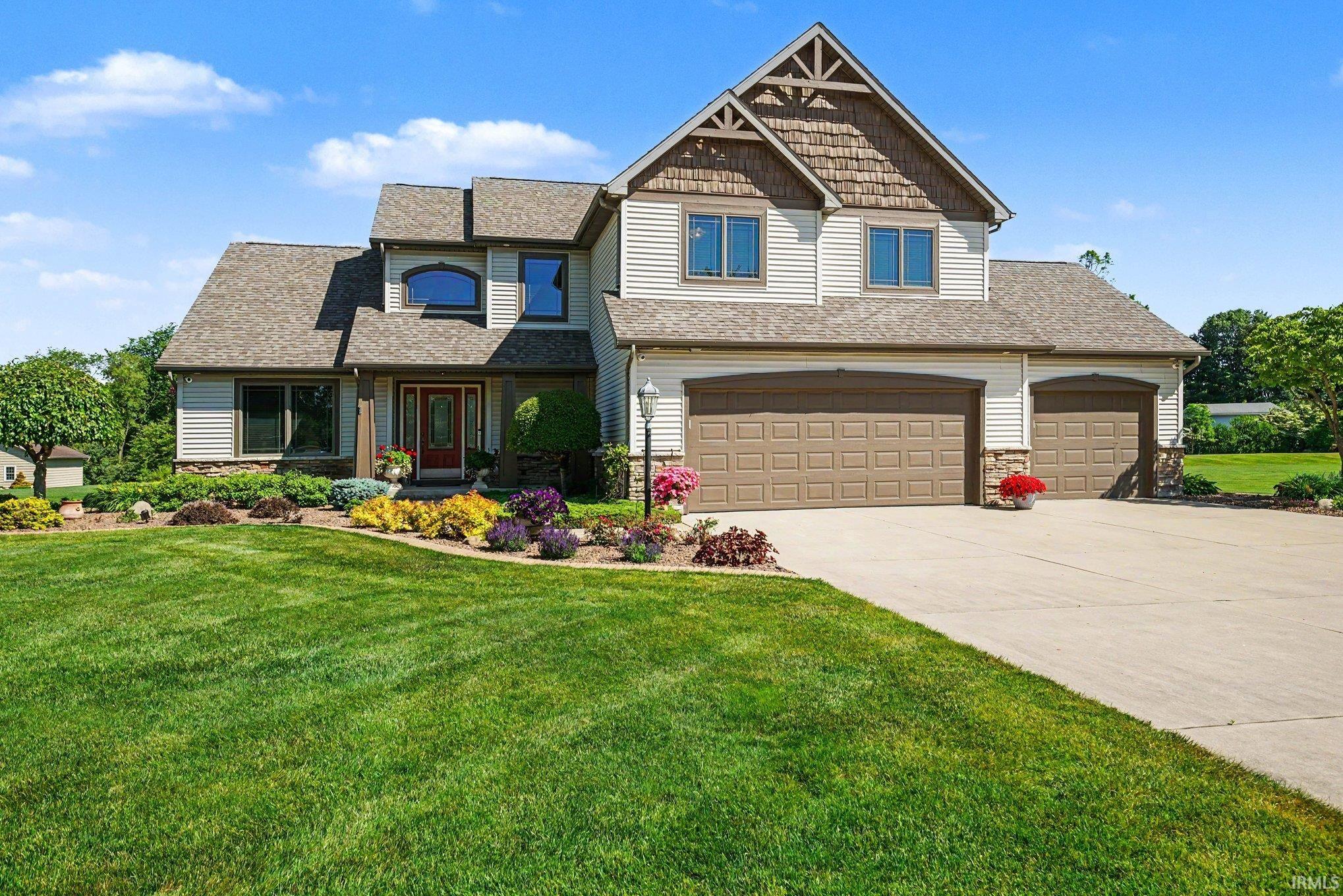 Traditional-style exterior featuring light-colored siding, a prominent front entry with a red door, a multi-car garage with brown doors, a paved driveway, and mature landscaping